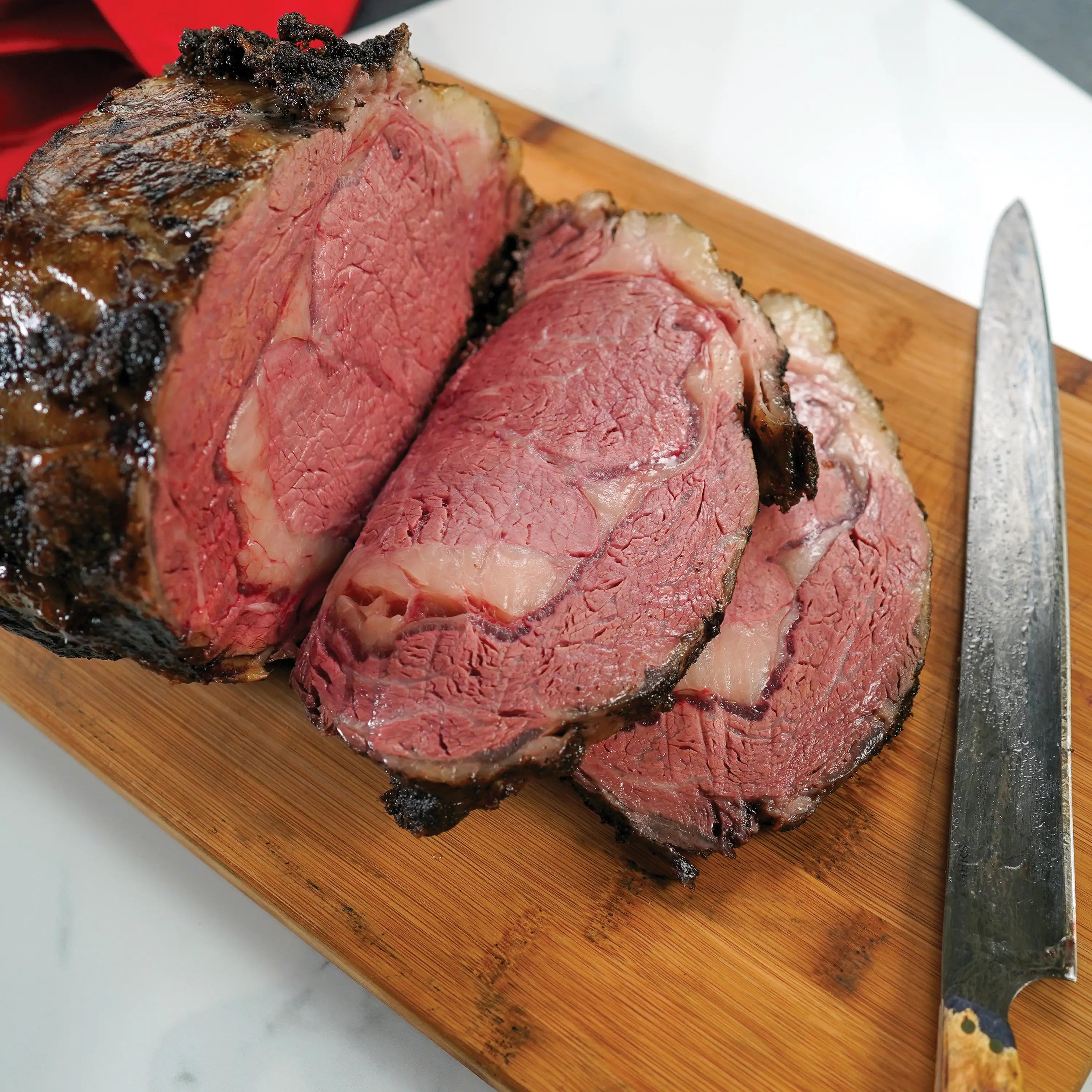 Thick slices of medium-rare roast beef on a wooden cutting board with a carving knife beside them.