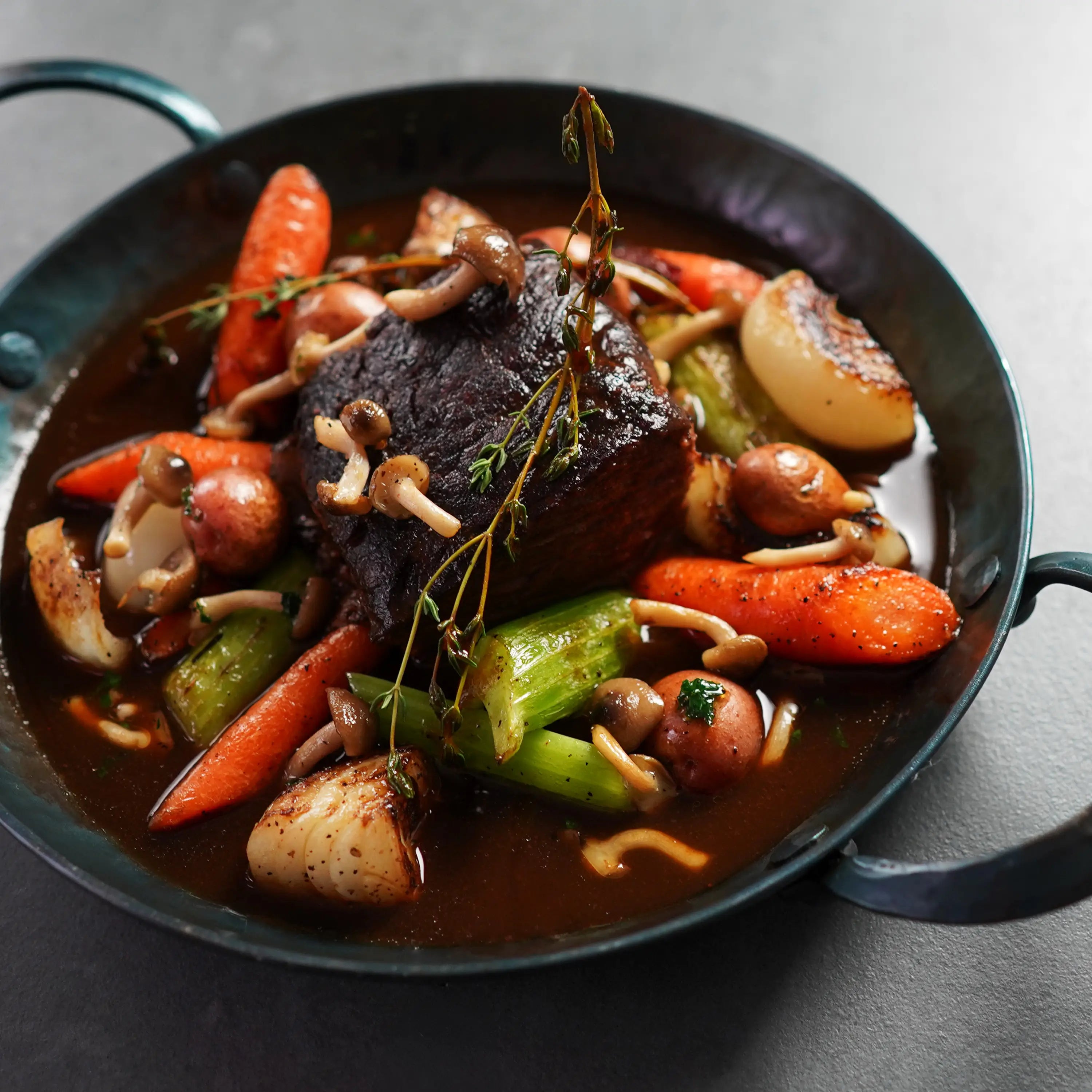 cooked steak in dark pan with vegetables and herb garnish