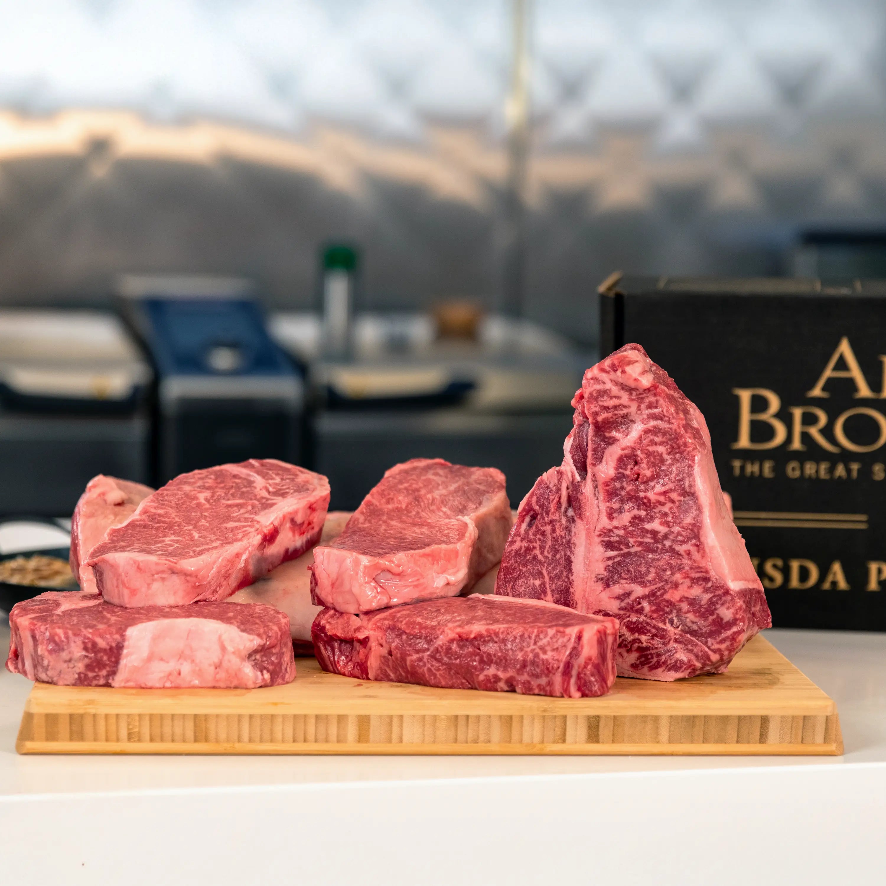 Several thick, well-marbled raw beef steaks on a wooden butcher’s block, with a partially visible USDA Prime sign in the background.