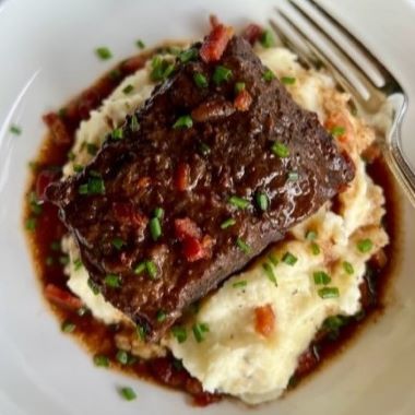 Plated dish of braised meat over mashed potatoes with a fork on the side.