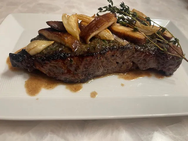 cooked steak on white plate with mushrooms on top and green garnish