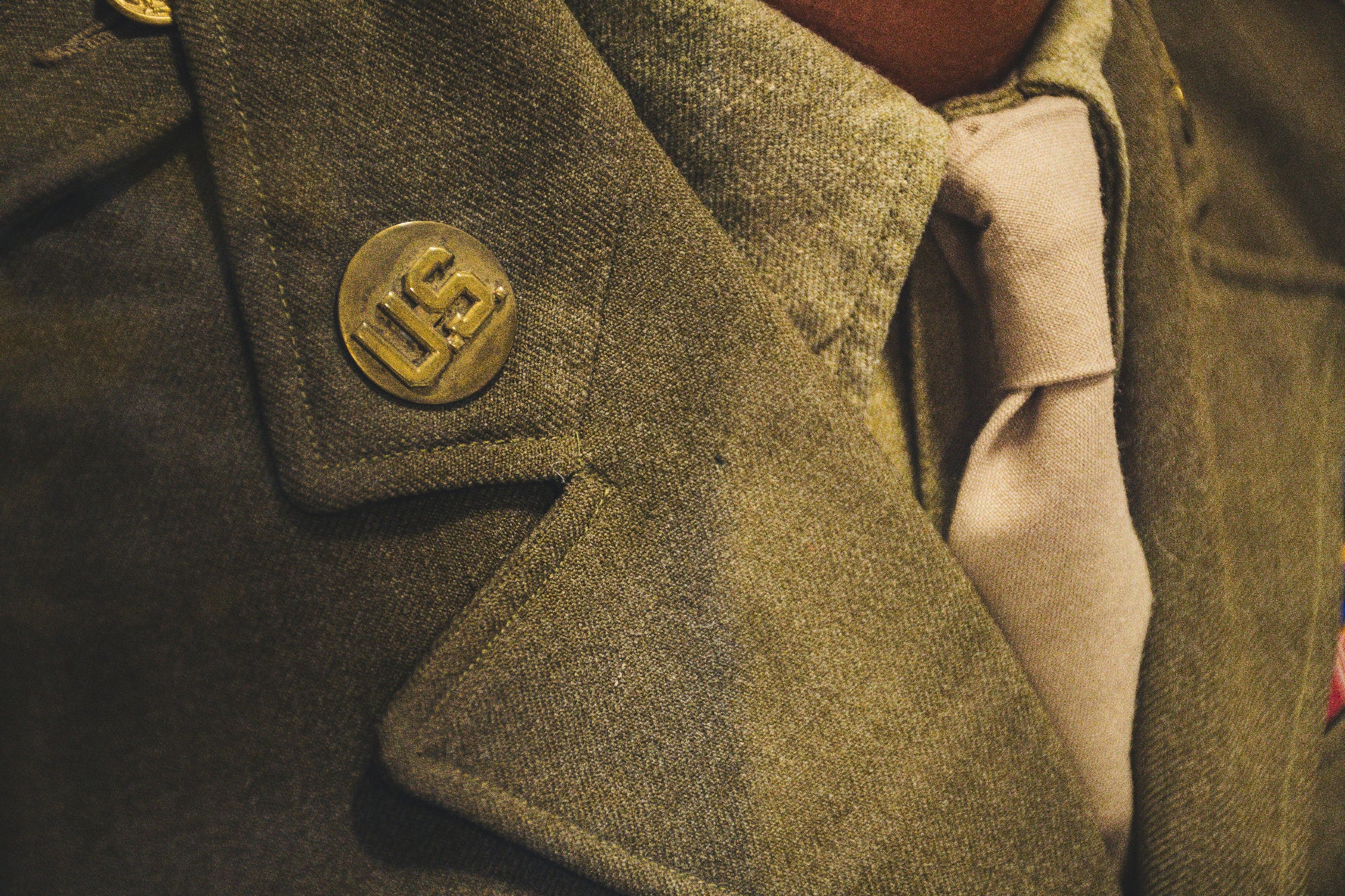 Close-up of a green military-style coat with a button and visible stitching details.