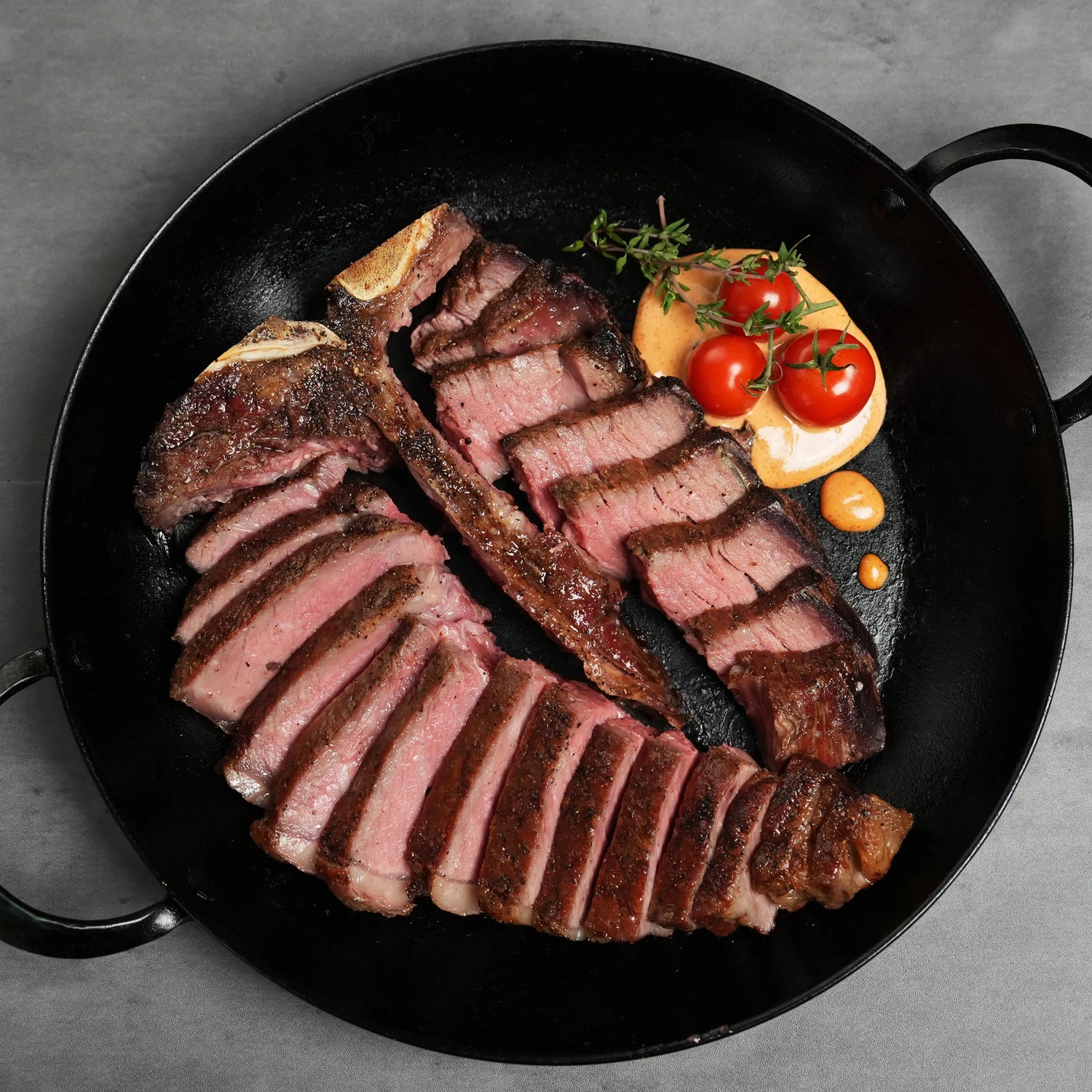 cooked and sliced steak in dark pan with red tomato garnish
