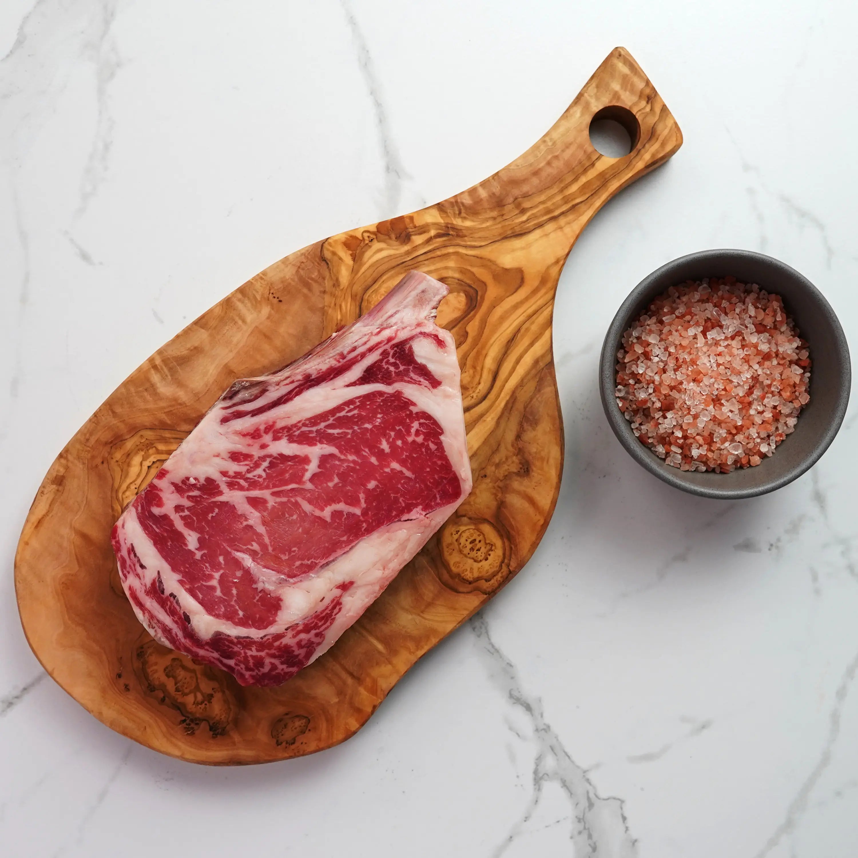 raw steak on wood board with pink salt in container on light surface
