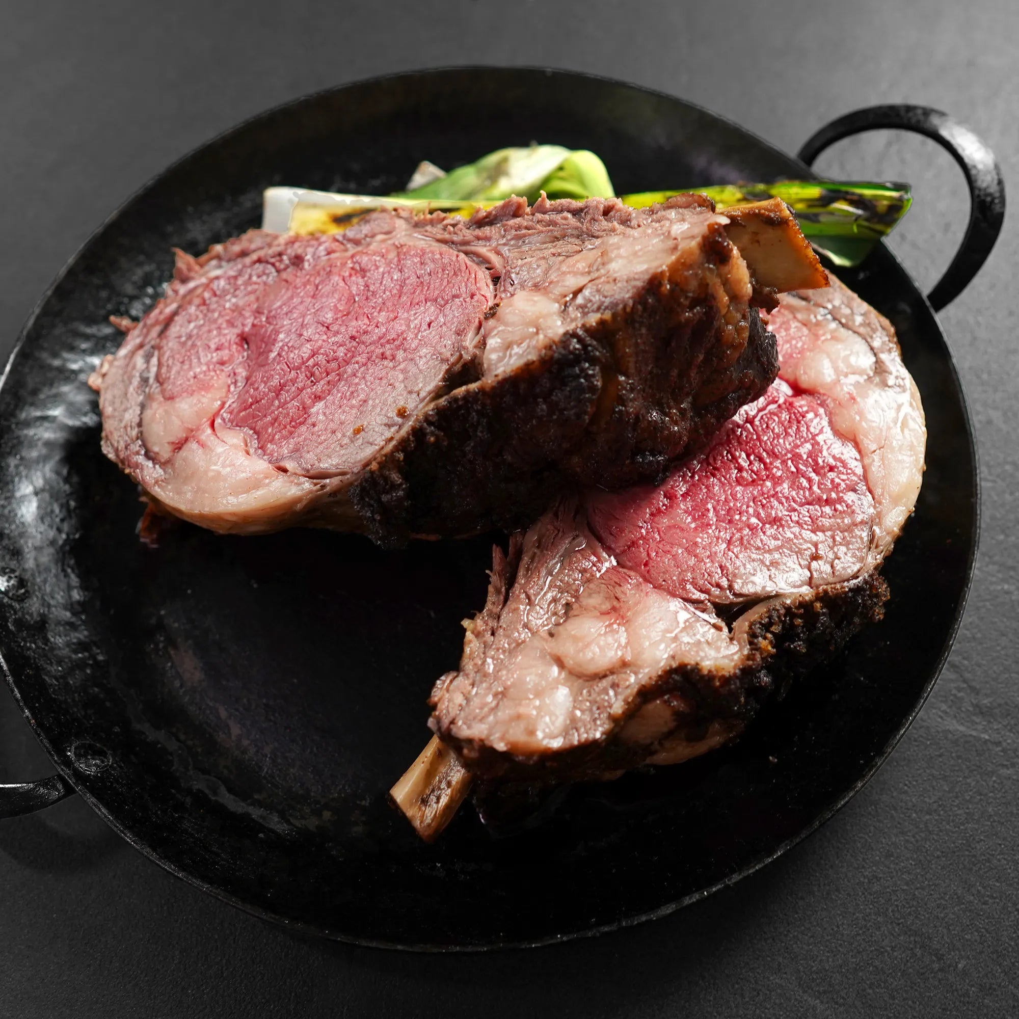 cooked rack of lamb cut in half on cast iron pan with green garnish