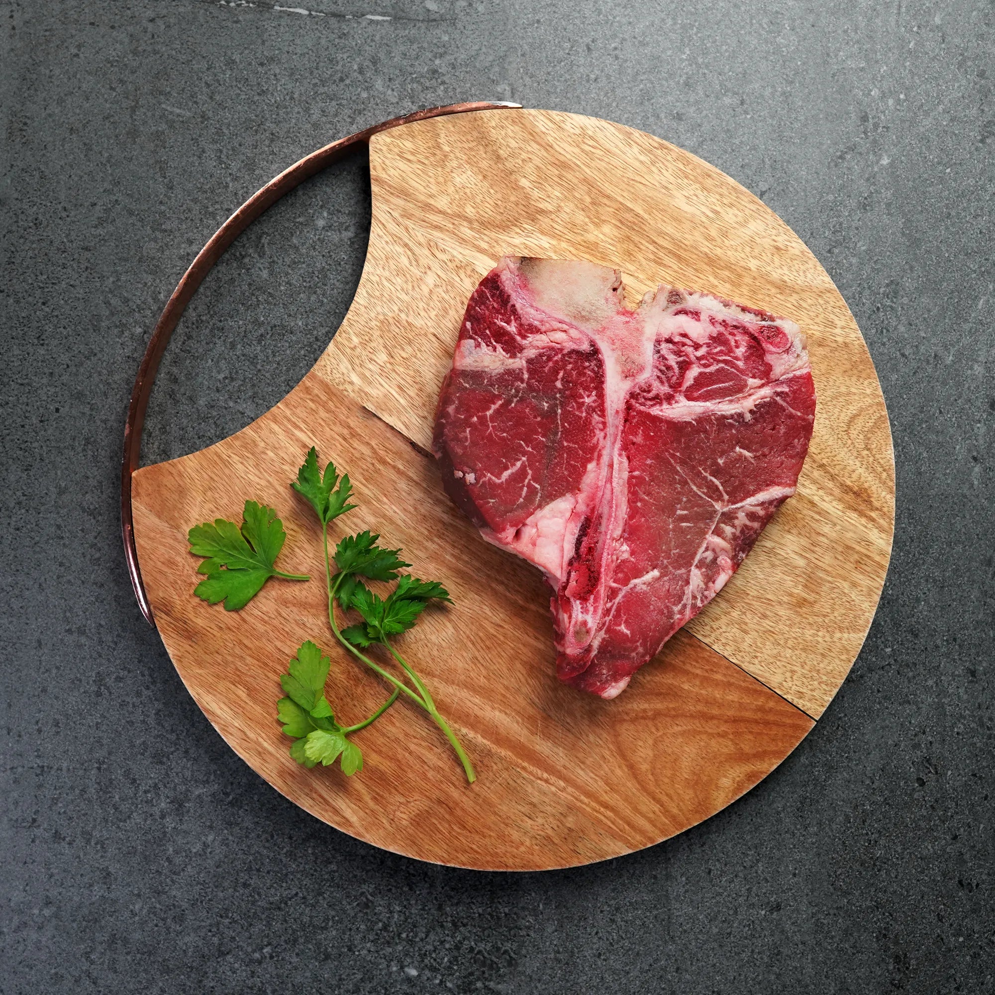 raw porterhouse steak on round wood board with green garnish
