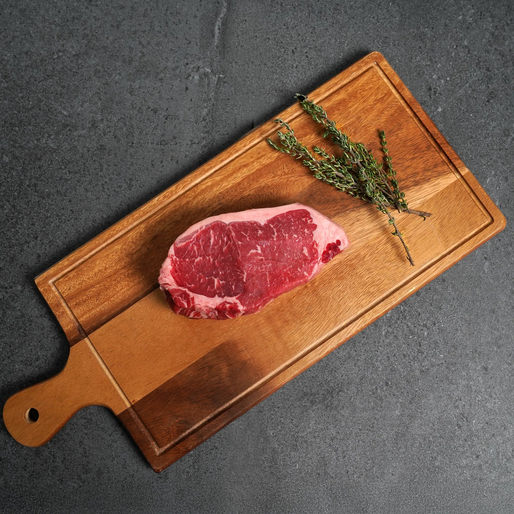 raw steak on rectangle wood board with green garnish
