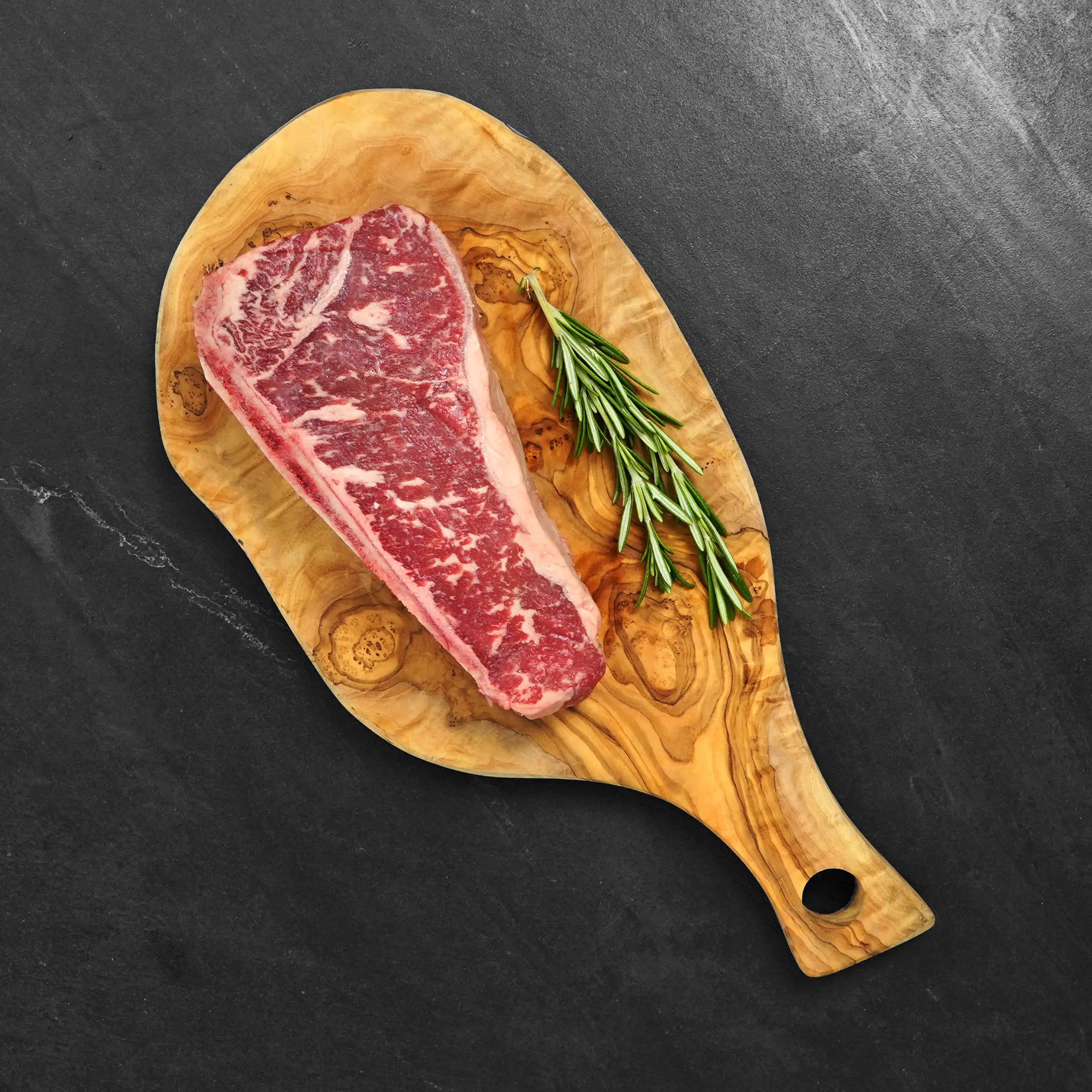 raw steak on wood board with green garnish