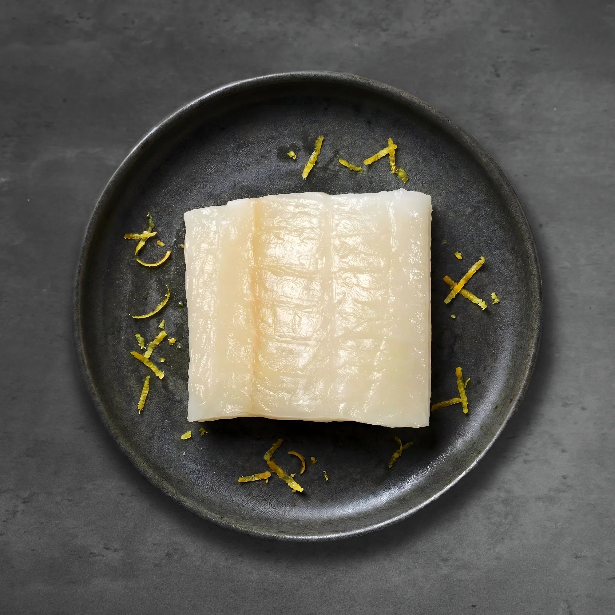 raw white fish on black plate with yellow garnish
