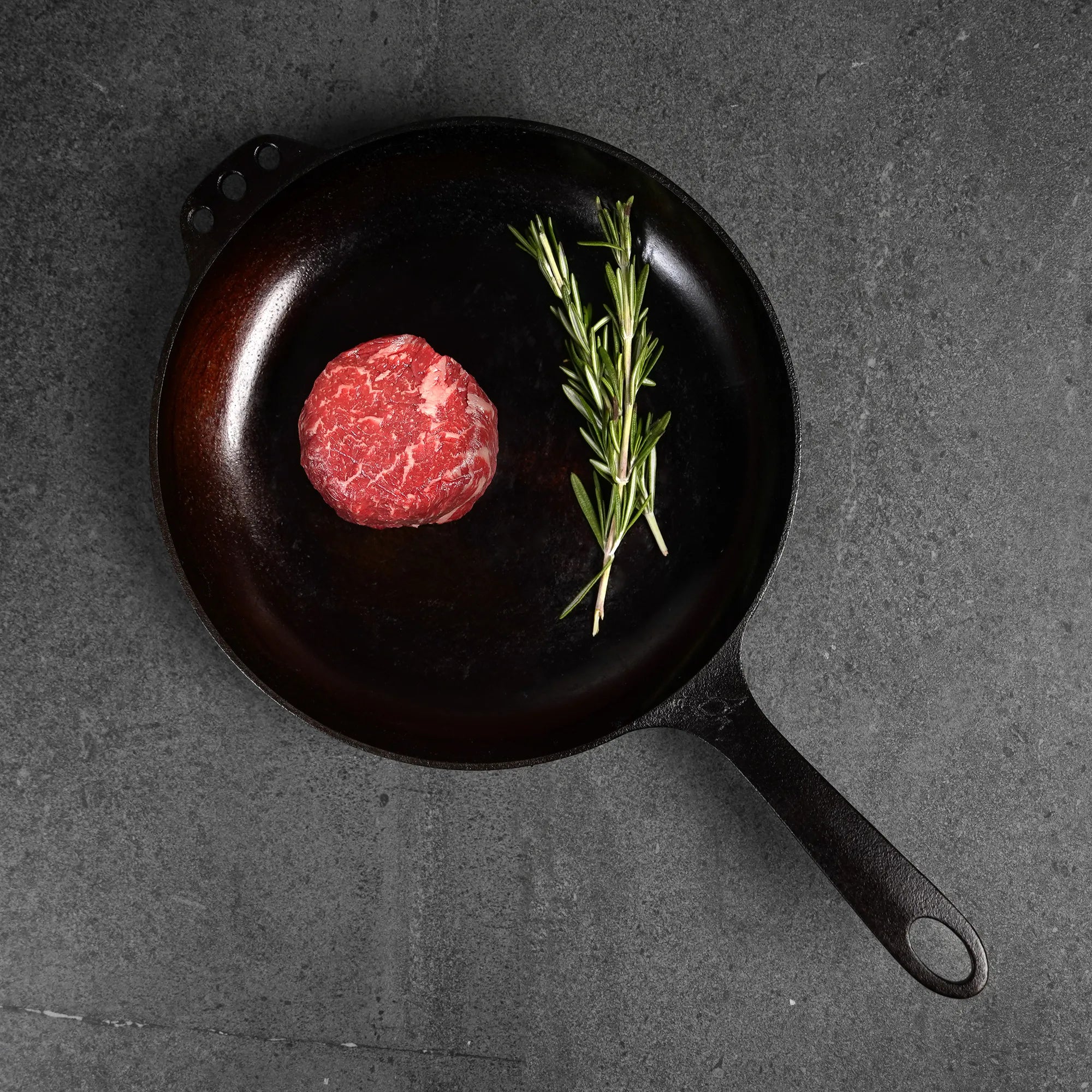 raw steak on cast iron pan with rosemary garnish