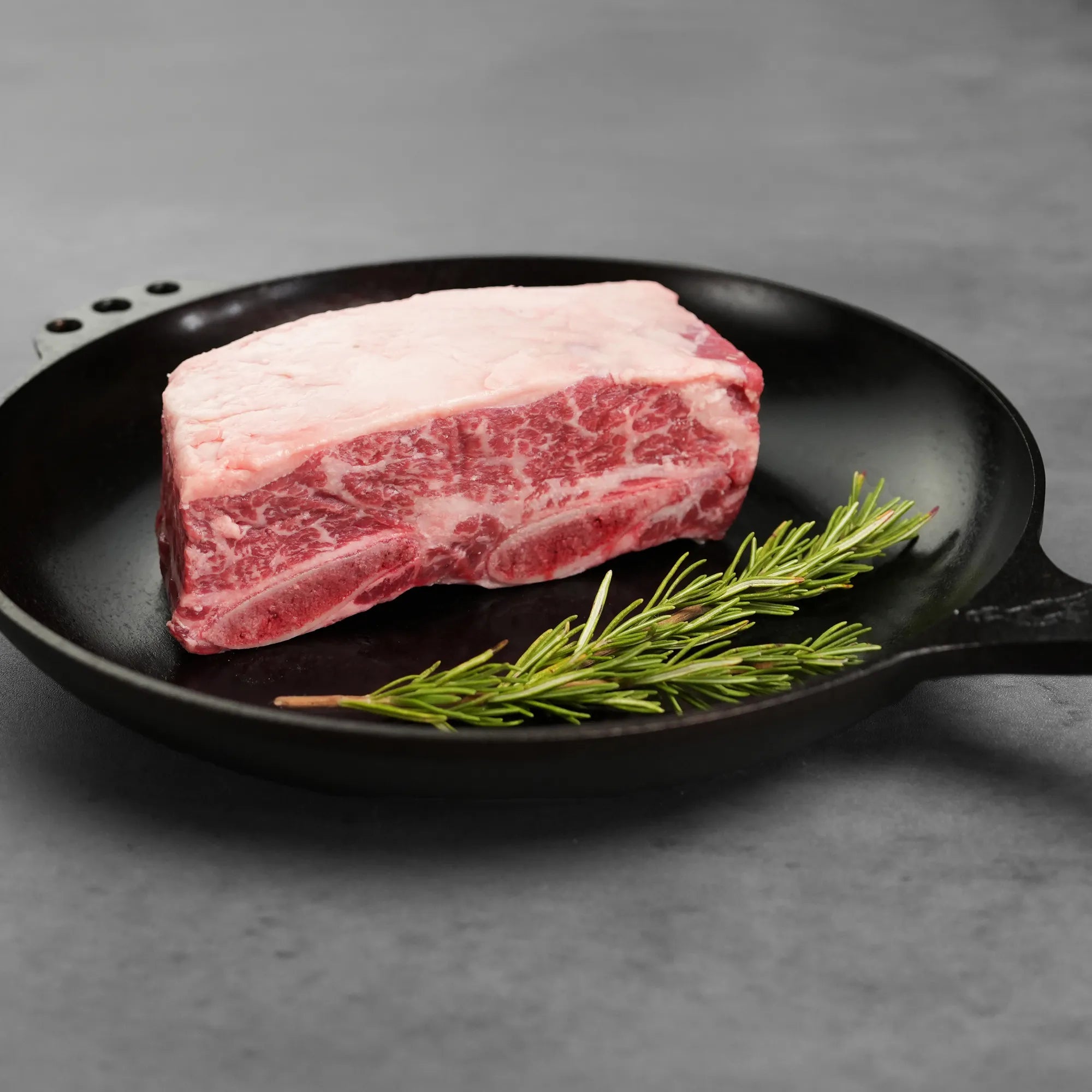 raw meat on black pan with green garnish on grey surface