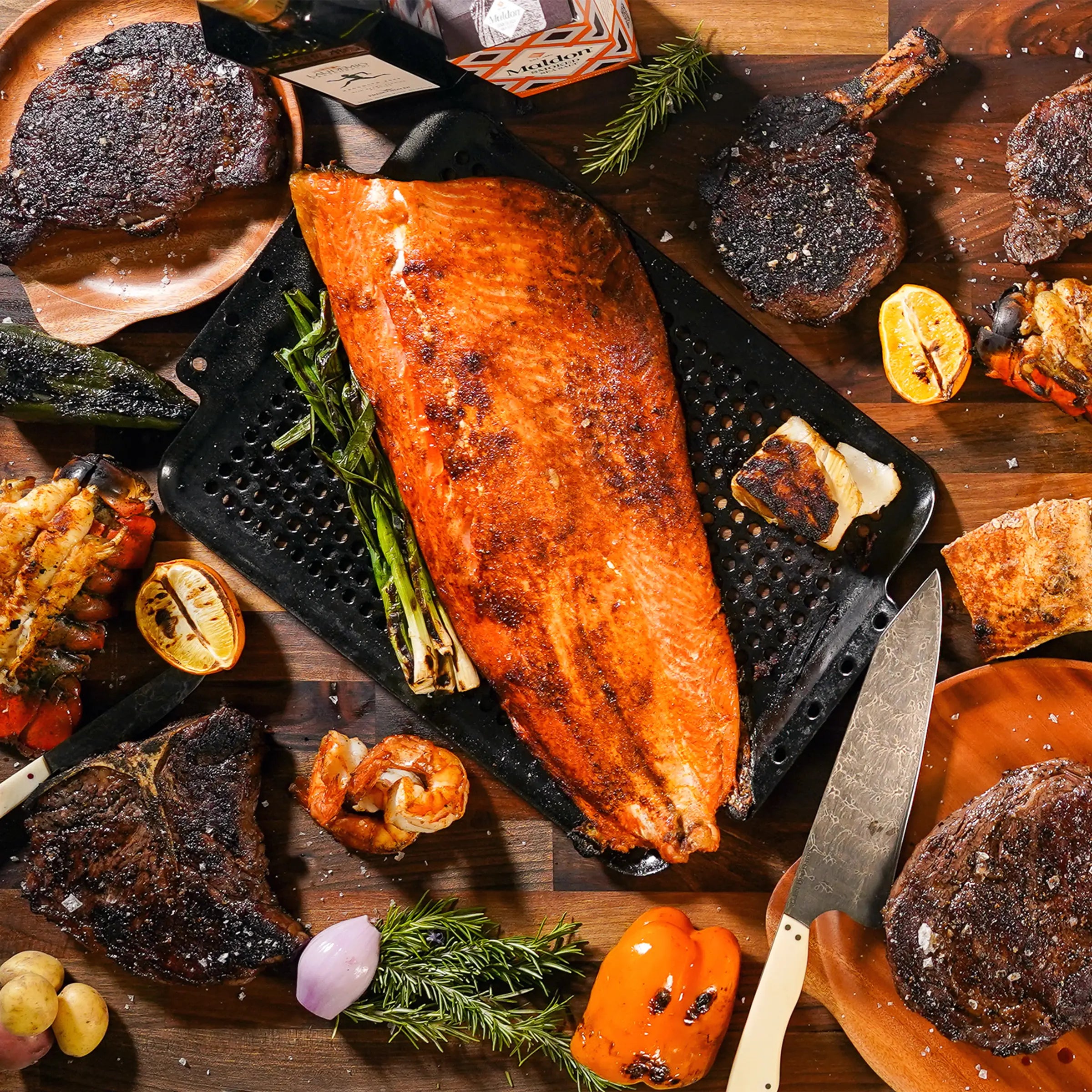 cooked steaks and fish filet on wood board with garnish and knife