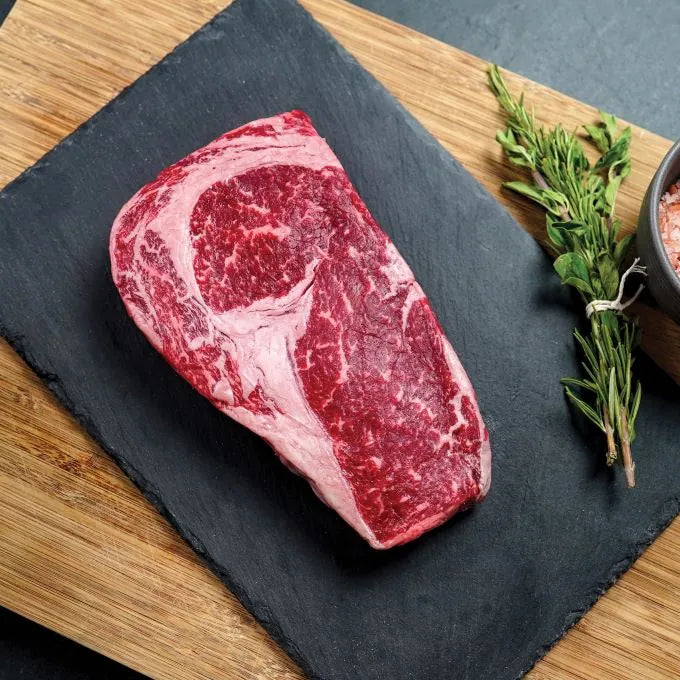 raw steak on black slate with green garnish on wood board