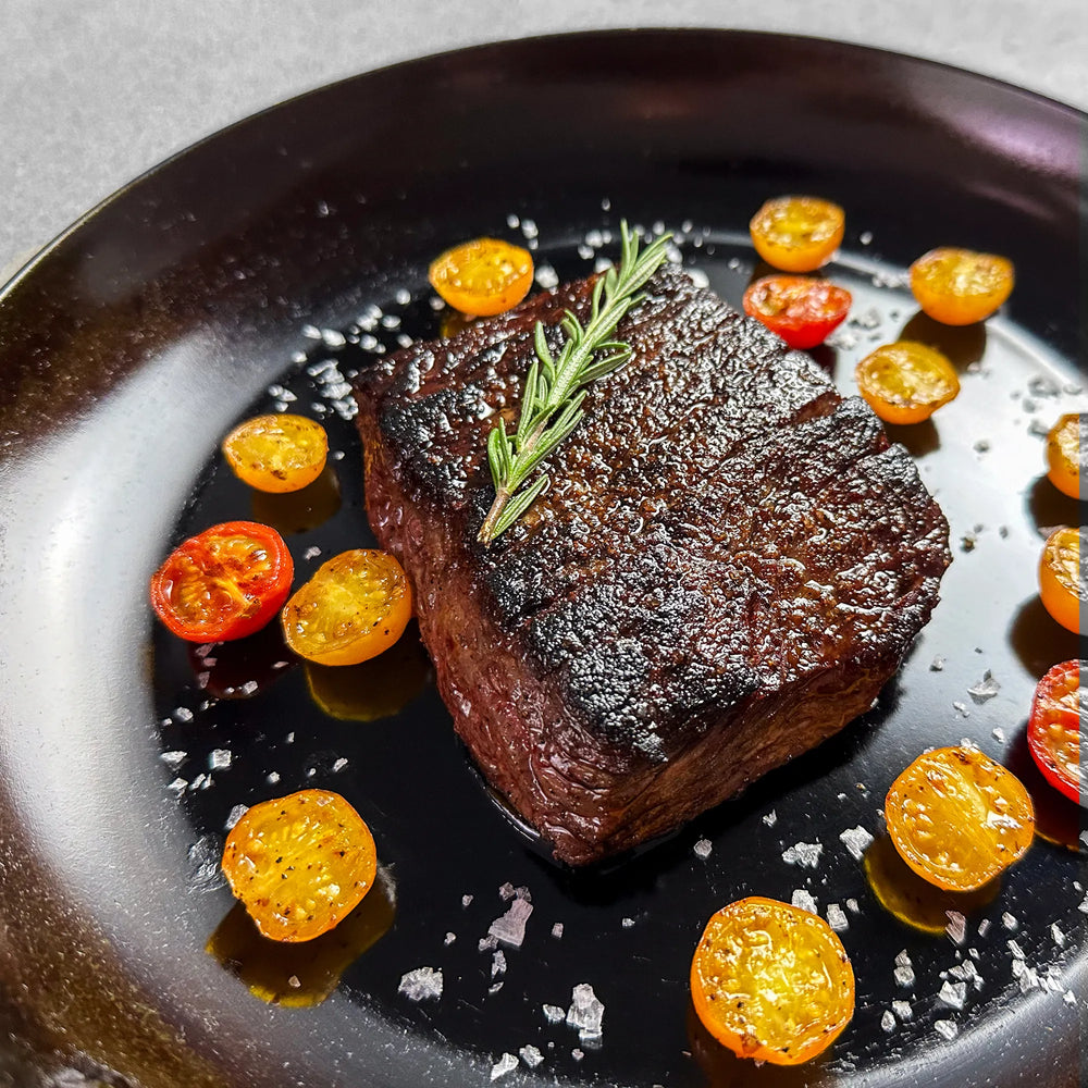 Westholme Australian Wagyu Bavette Steak seared on a dark plate, garnished with rosemary, cherry tomatoes, and sprinkled with flaky sea salt, showcasing its marbled texture.