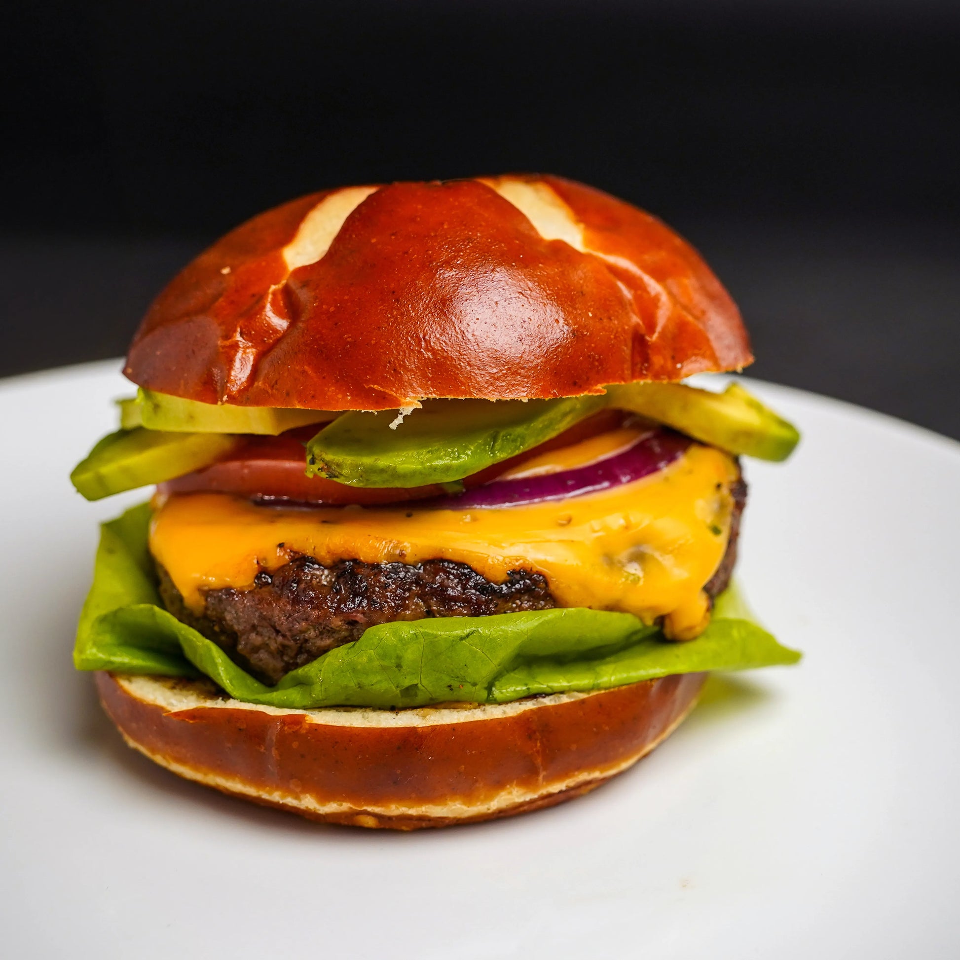 All-American Combo featuring a juicy cheeseburger with cheddar, avocado, red onion, tomato, and lettuce on a pretzel roll, showcasing premium steak burger quality.