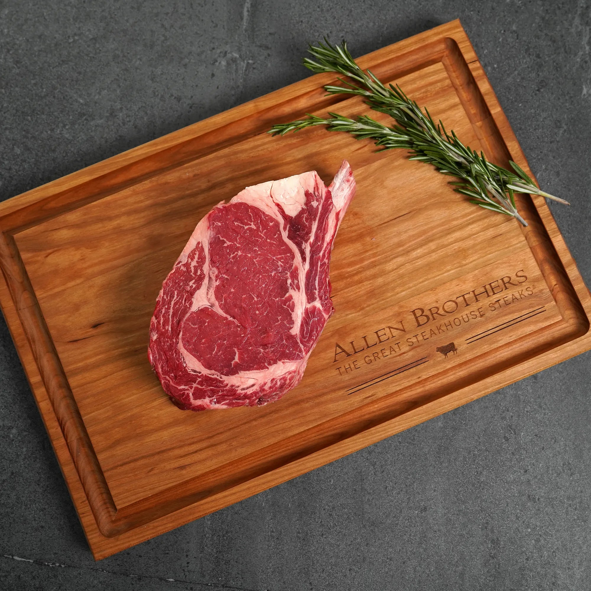 Raw steak on wood board with Allen Brother Logo and rosemary sprig as garnish