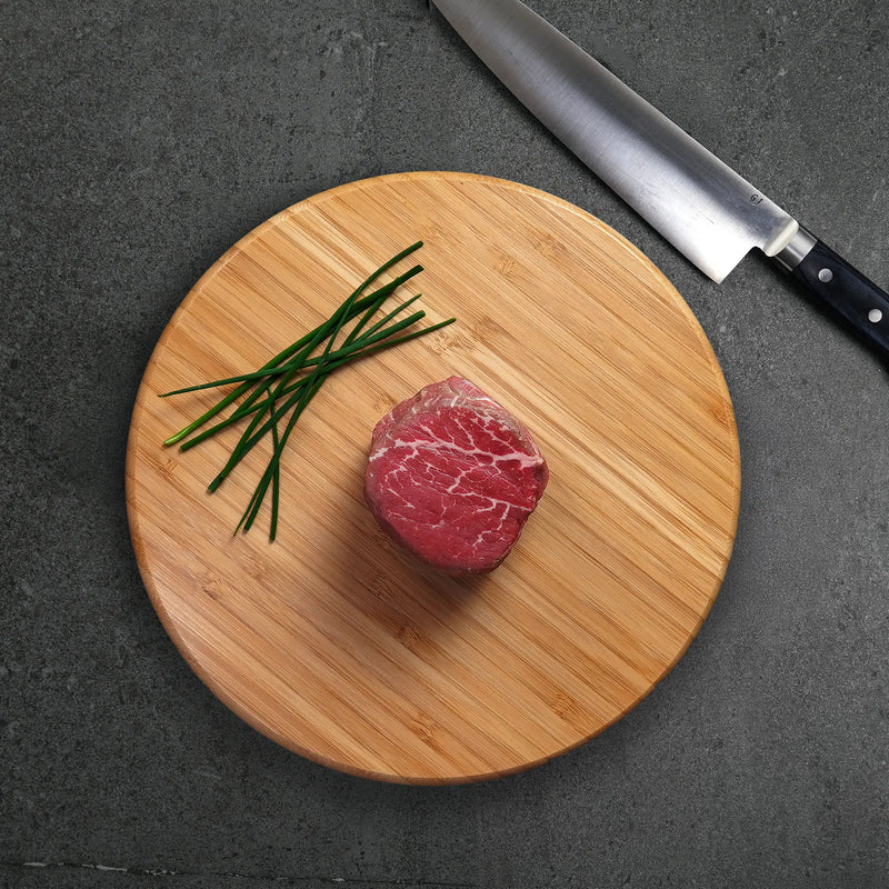 King & Queen Choice Angus Combo featuring a raw filet steak and chives on a bamboo board, with a stainless-steel chef’s knife nearby.