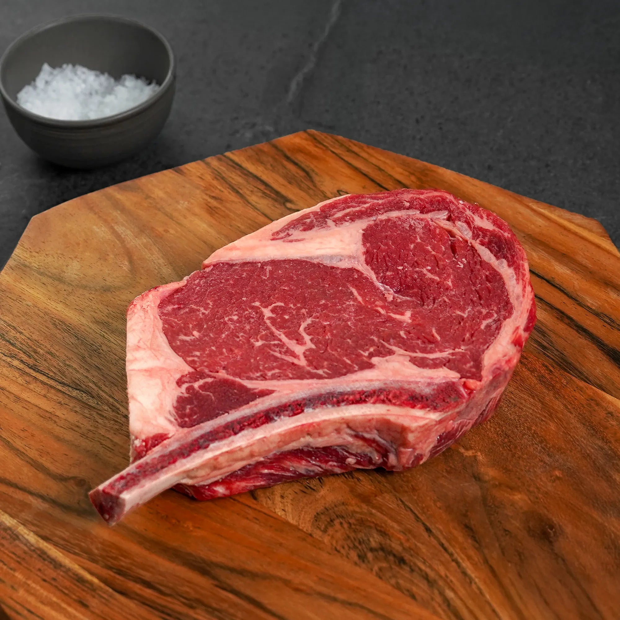 Raw steak with bone on wood with salt container