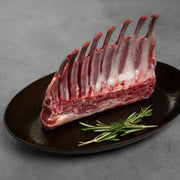 Allen Brothers Domestic all natural rack of lamb raw standing on a black plate with rosemary