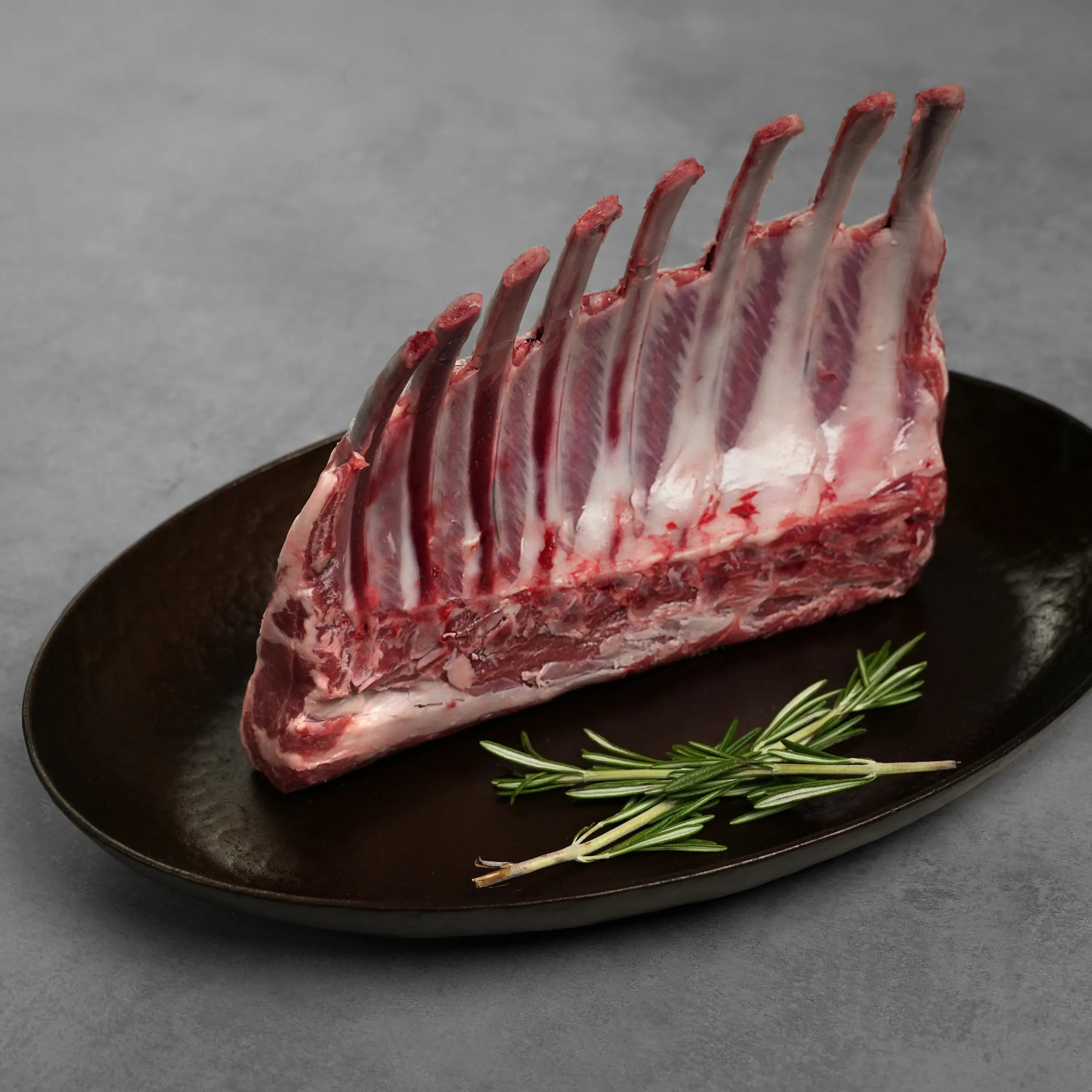 Allen Brothers Domestic all natural rack of lamb raw standing on a black plate with rosemary