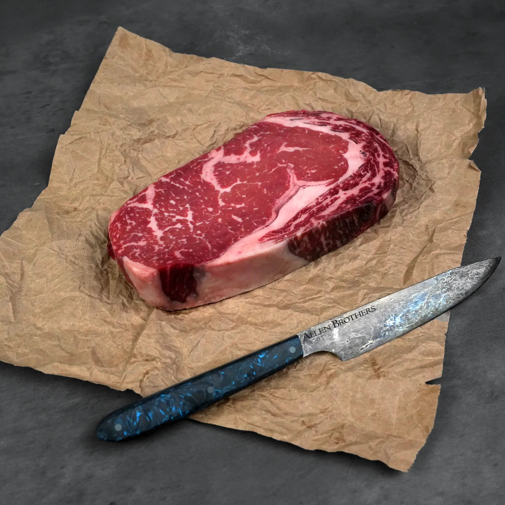 Dry Aged Prime Boneless Ribeye Steak on butcher's paper with an Allen Brothers knife, showcasing its rich marbling, ideal for steak connoisseurs.