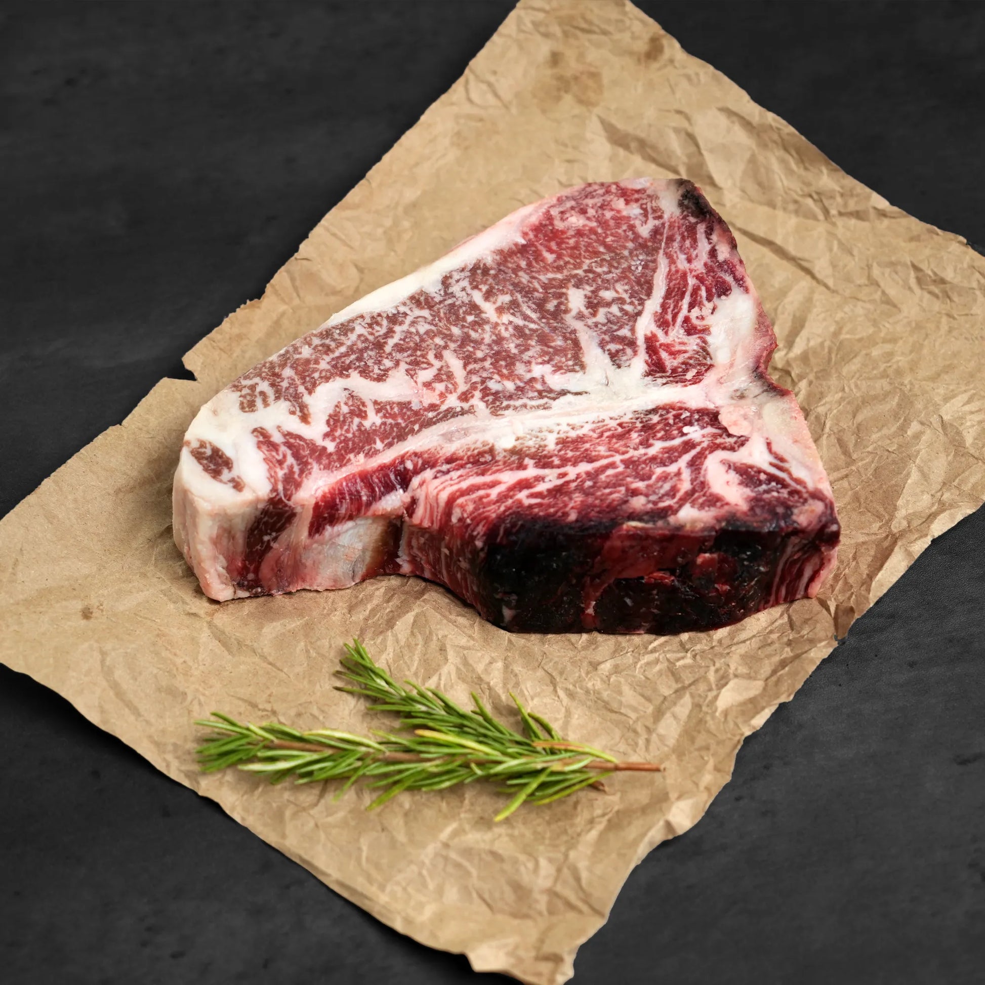 Raw steak on butchers paper with rosemary as garnish