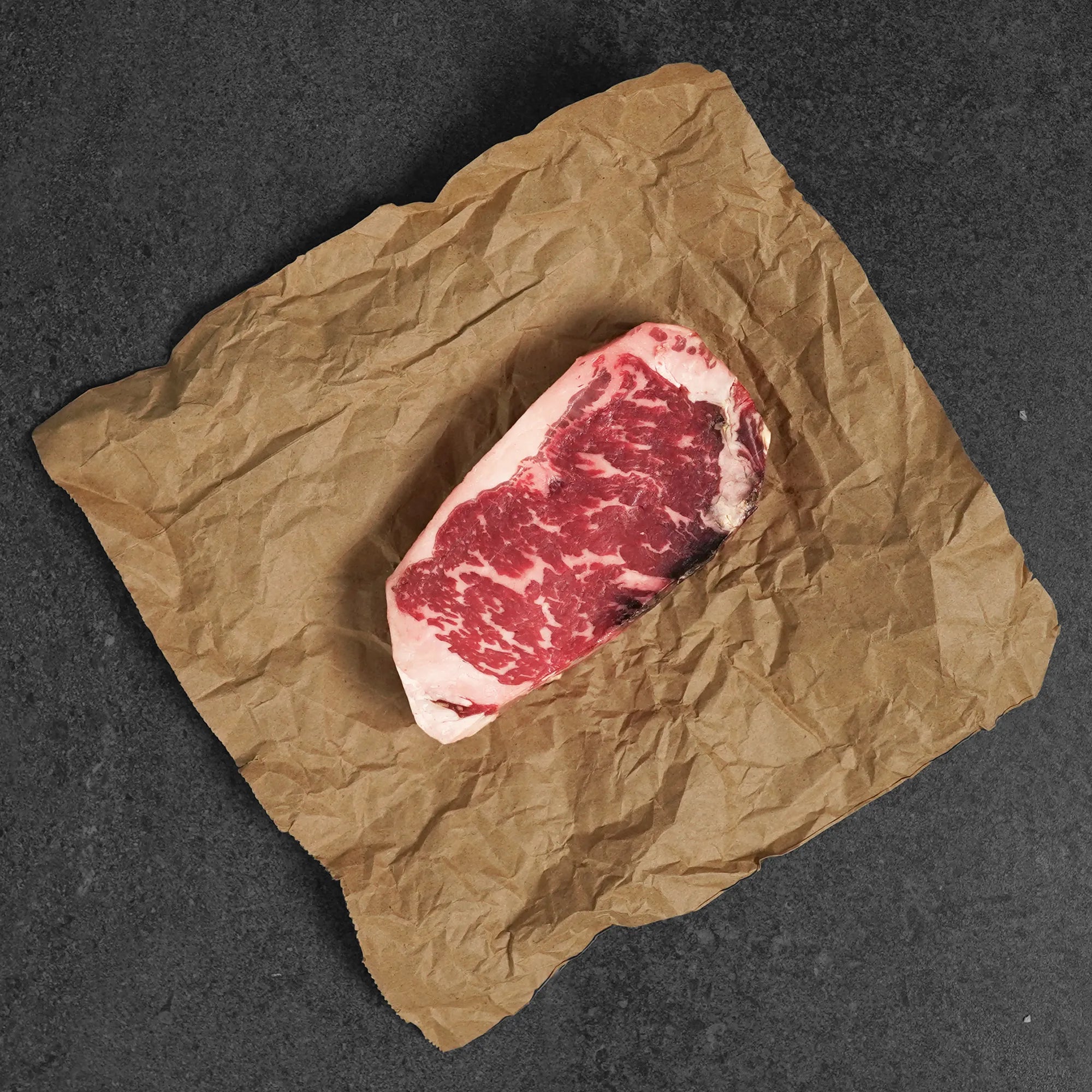Raw steak on crumpled brown paper against a dark background