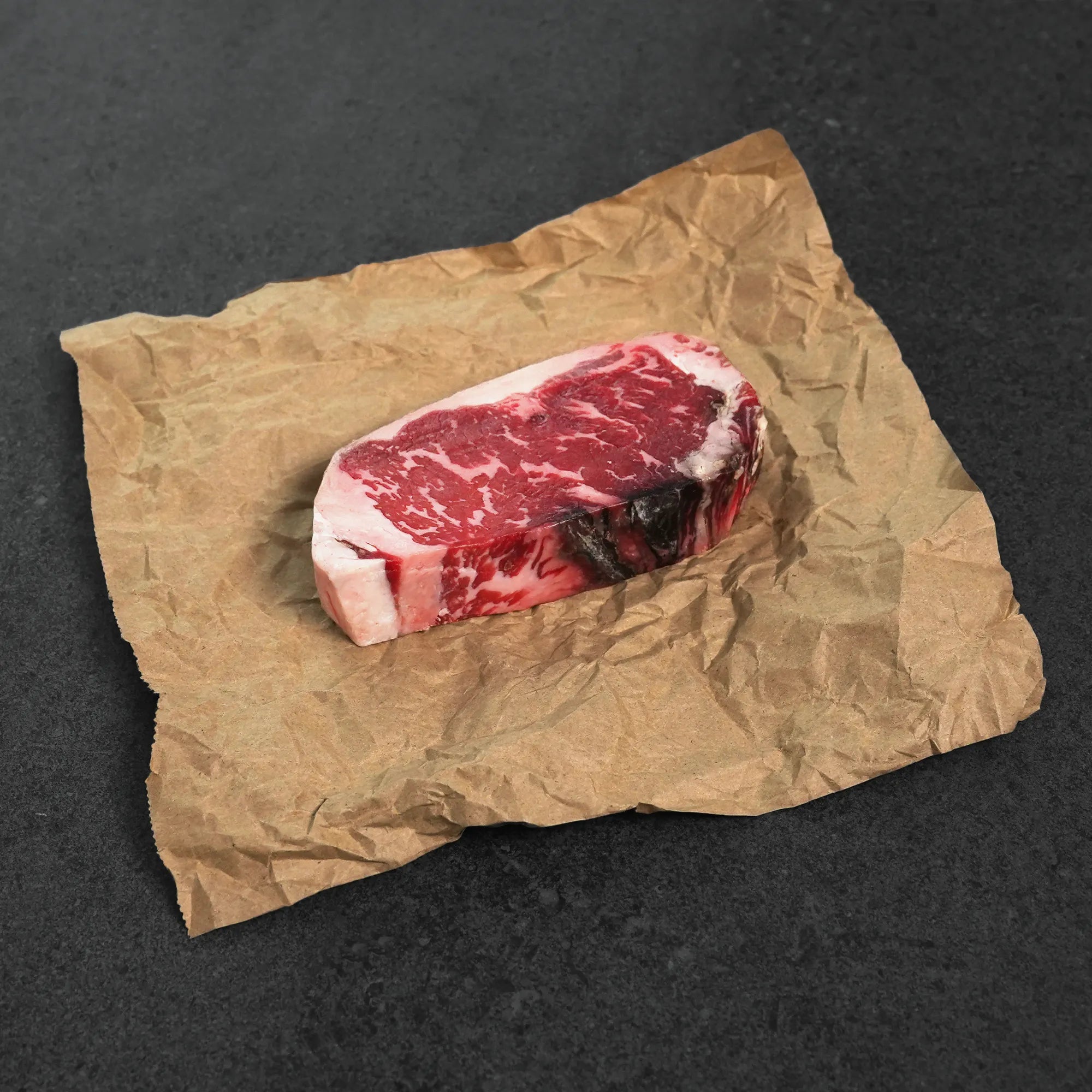 Raw steak on crumpled brown paper against a dark background