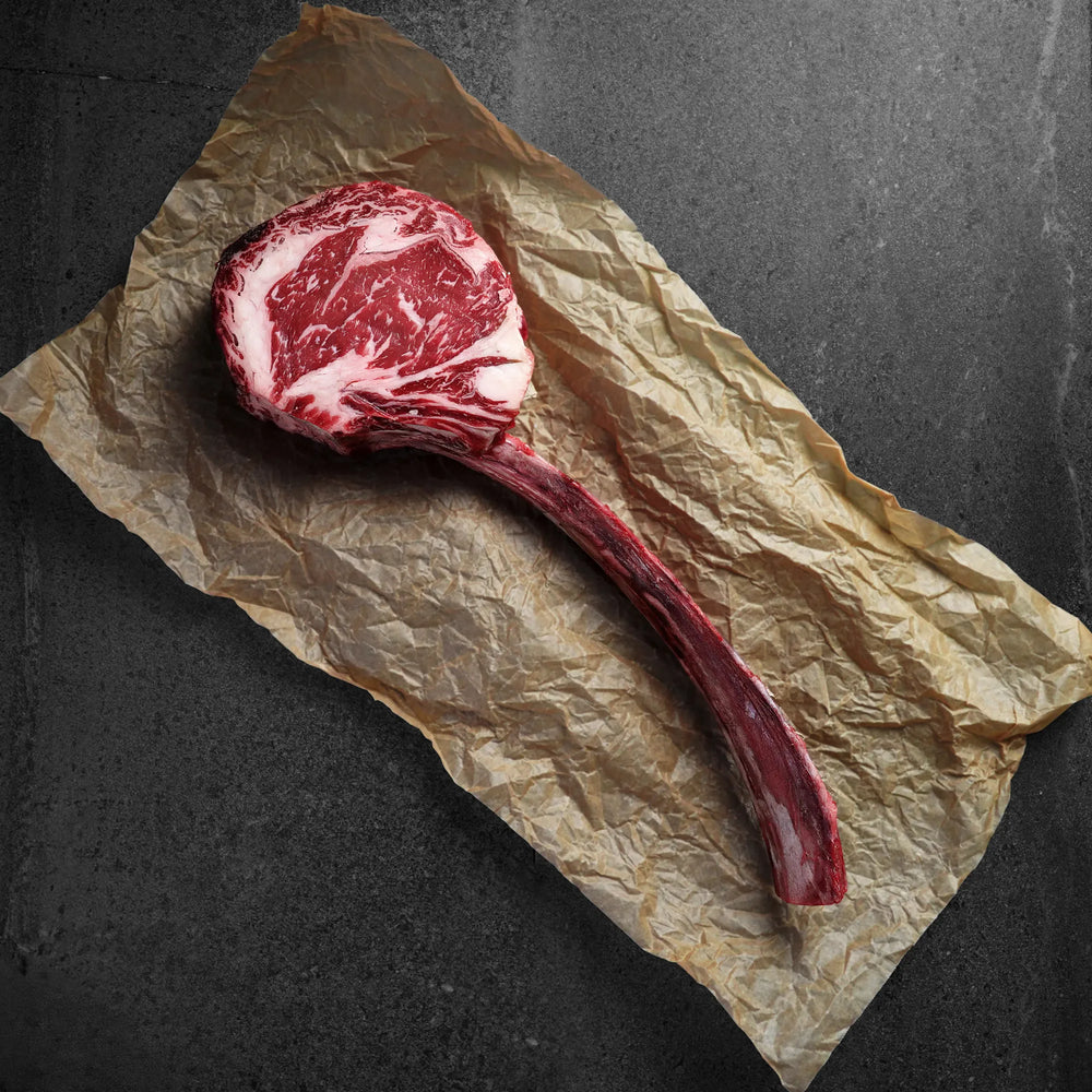 Raw ribeye steak on a crumpled piece of brown paper against a dark background