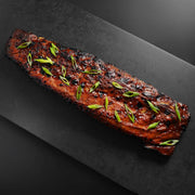 Heritage Duroc Pork Peeled Baby Back Rib, richly glazed and charred, garnished with scallions, presented on a dark platter, showcasing premium barbecue appeal.