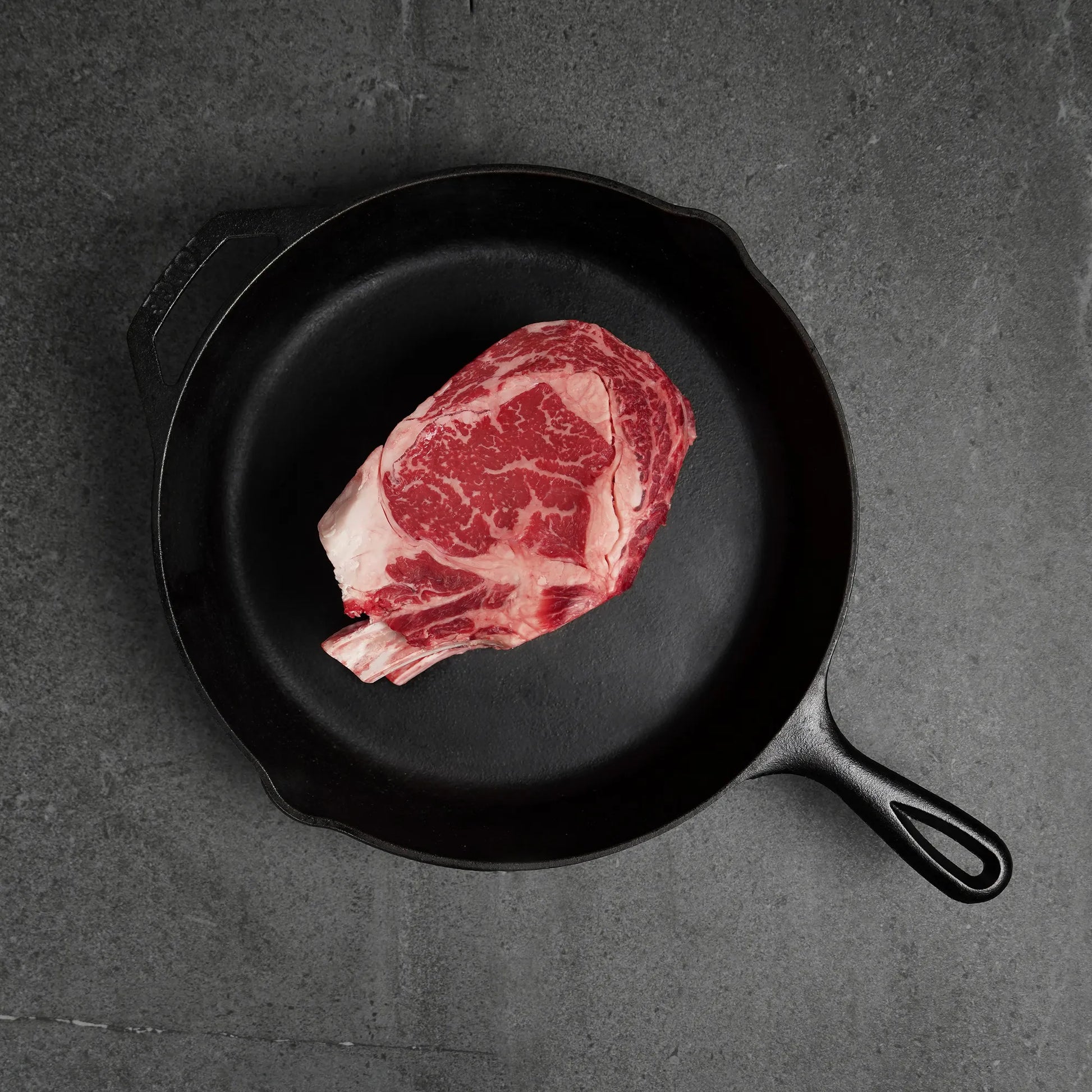 Raw bone in meat on black iron pan on a dark surface
