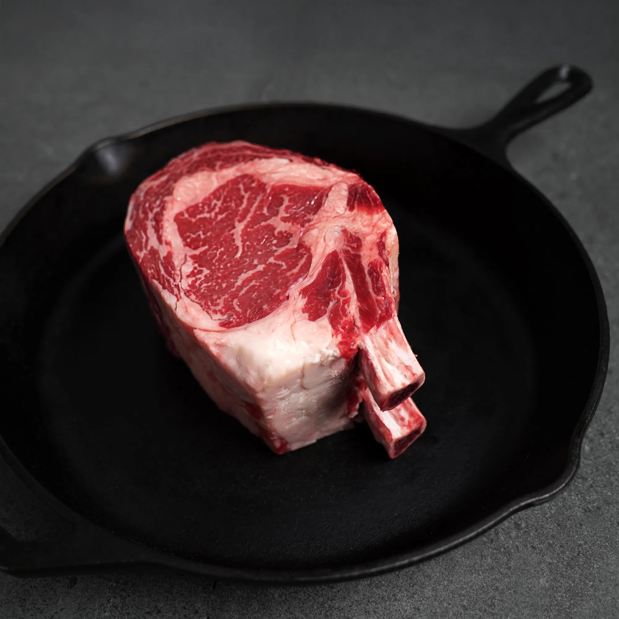 Raw ribeye steak on a black cast iron skillet against a dark background