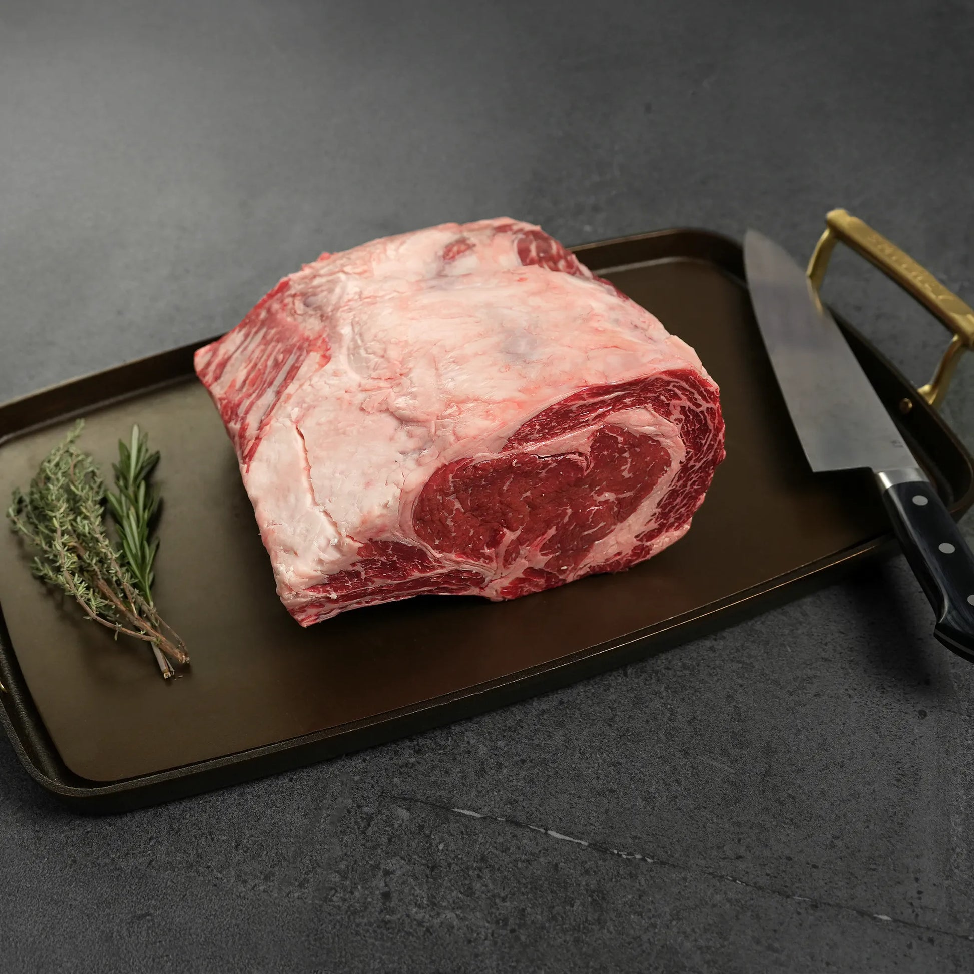 Raw meat on metal pan with gold handles and rosemary garnish