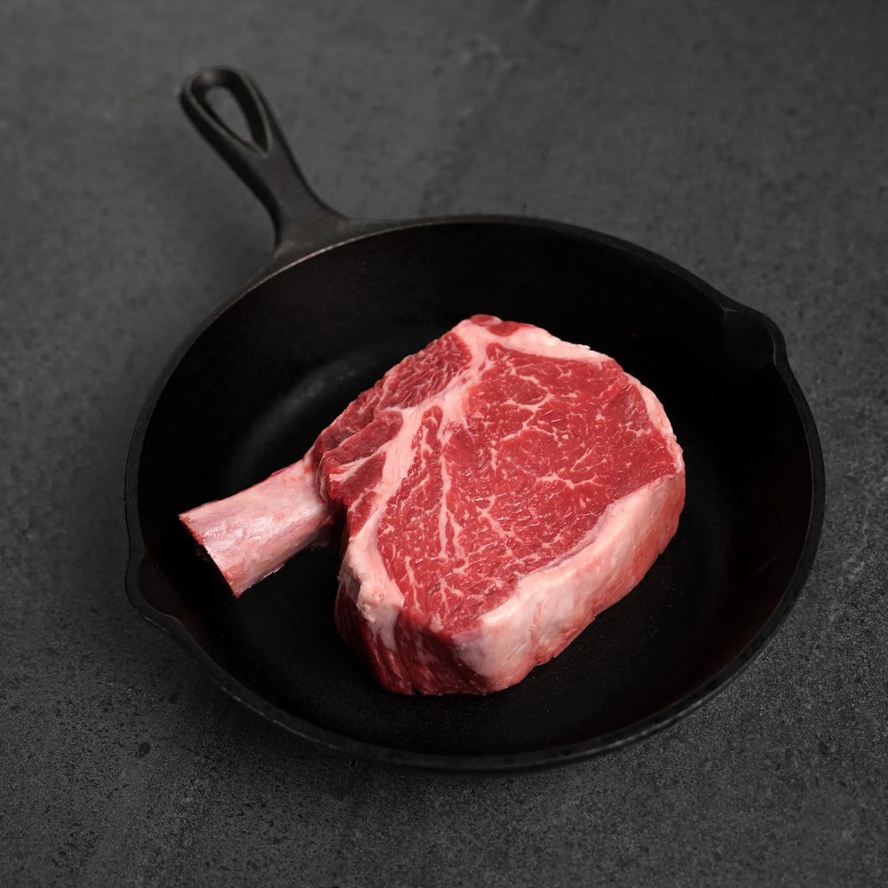 Raw ribeye steak in a cast iron skillet on a dark surface