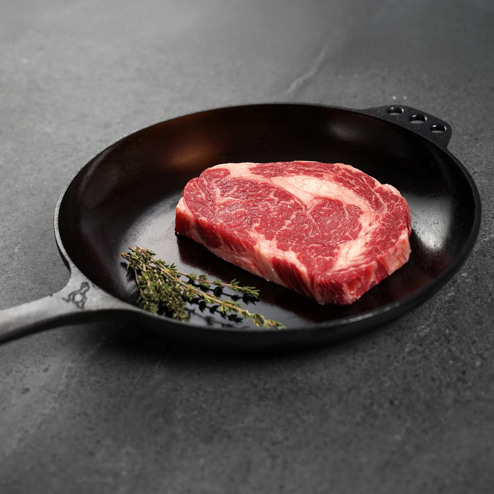 Raw steak in a cast iron skillet on a dark surface