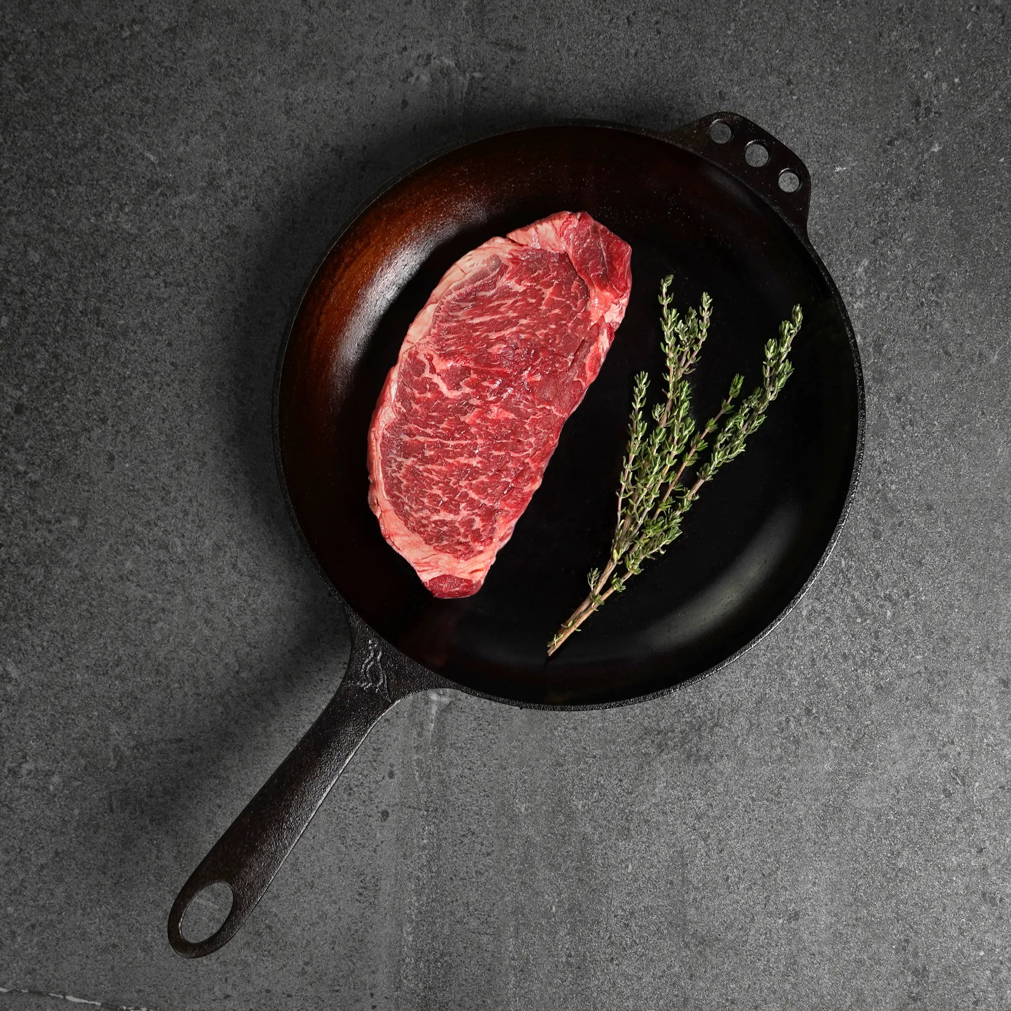Raw steak with herbs on a black cast iron skillet against a dark background