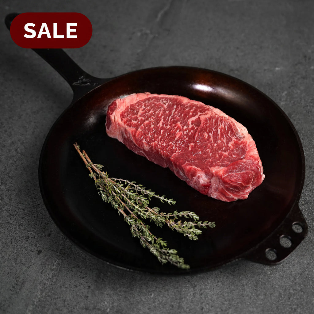 Raw steak on a black cast iron skillet with fresh herbs on a dark surface