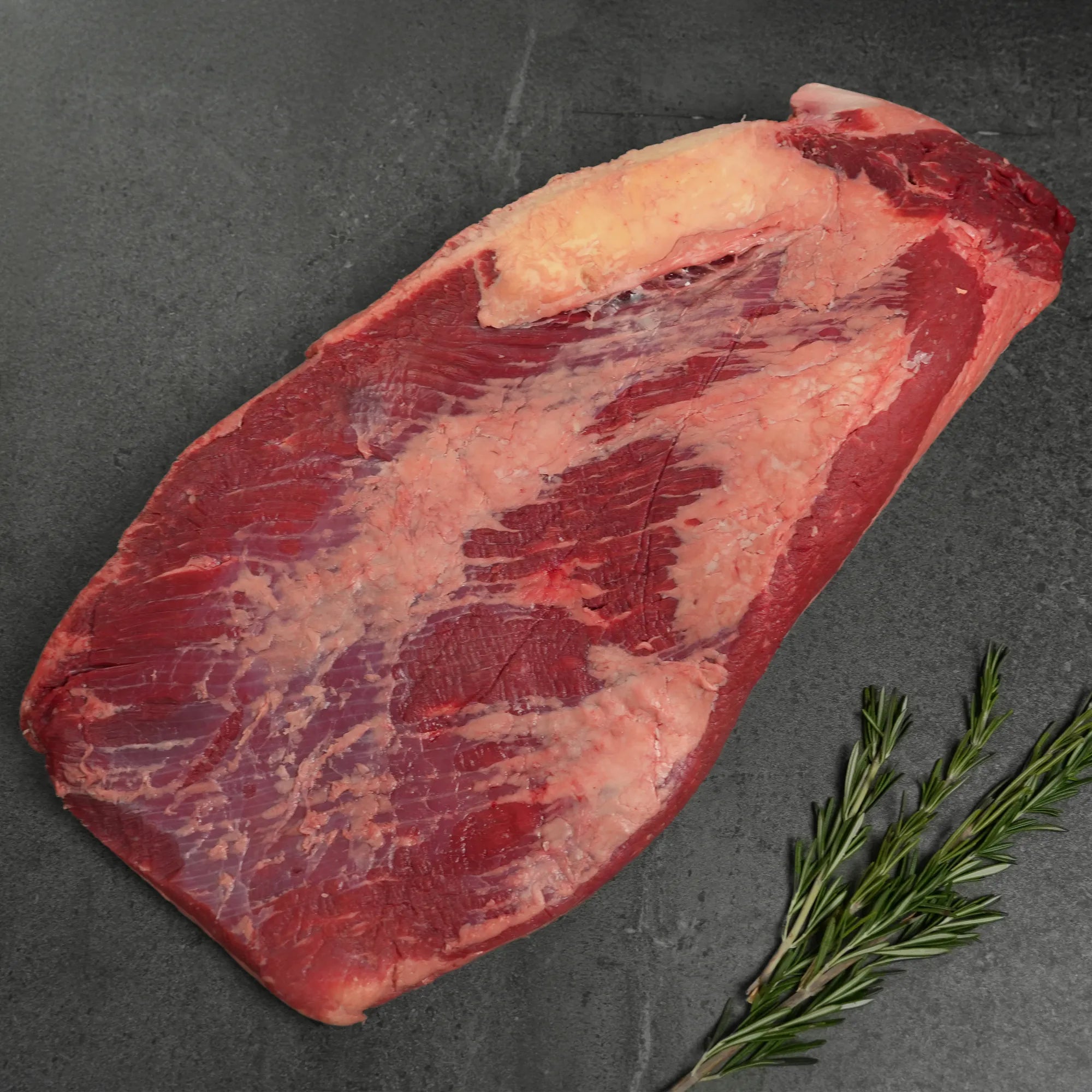 Raw meat on a dark surface with a sprig of rosemary