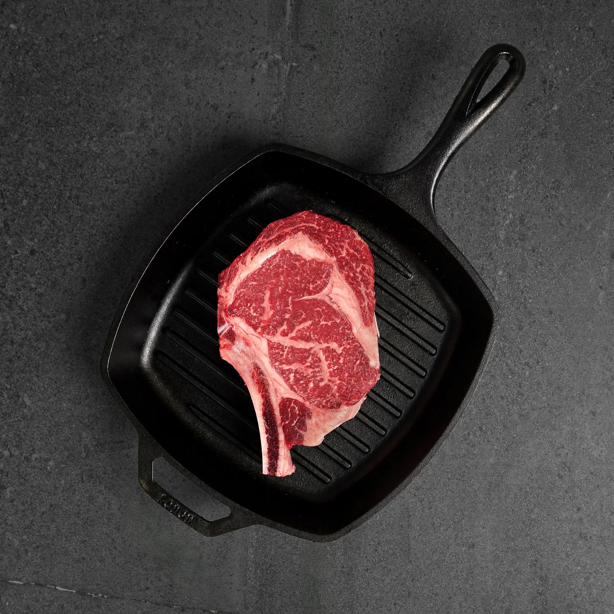 Raw steak in a black grill pan on a dark surface