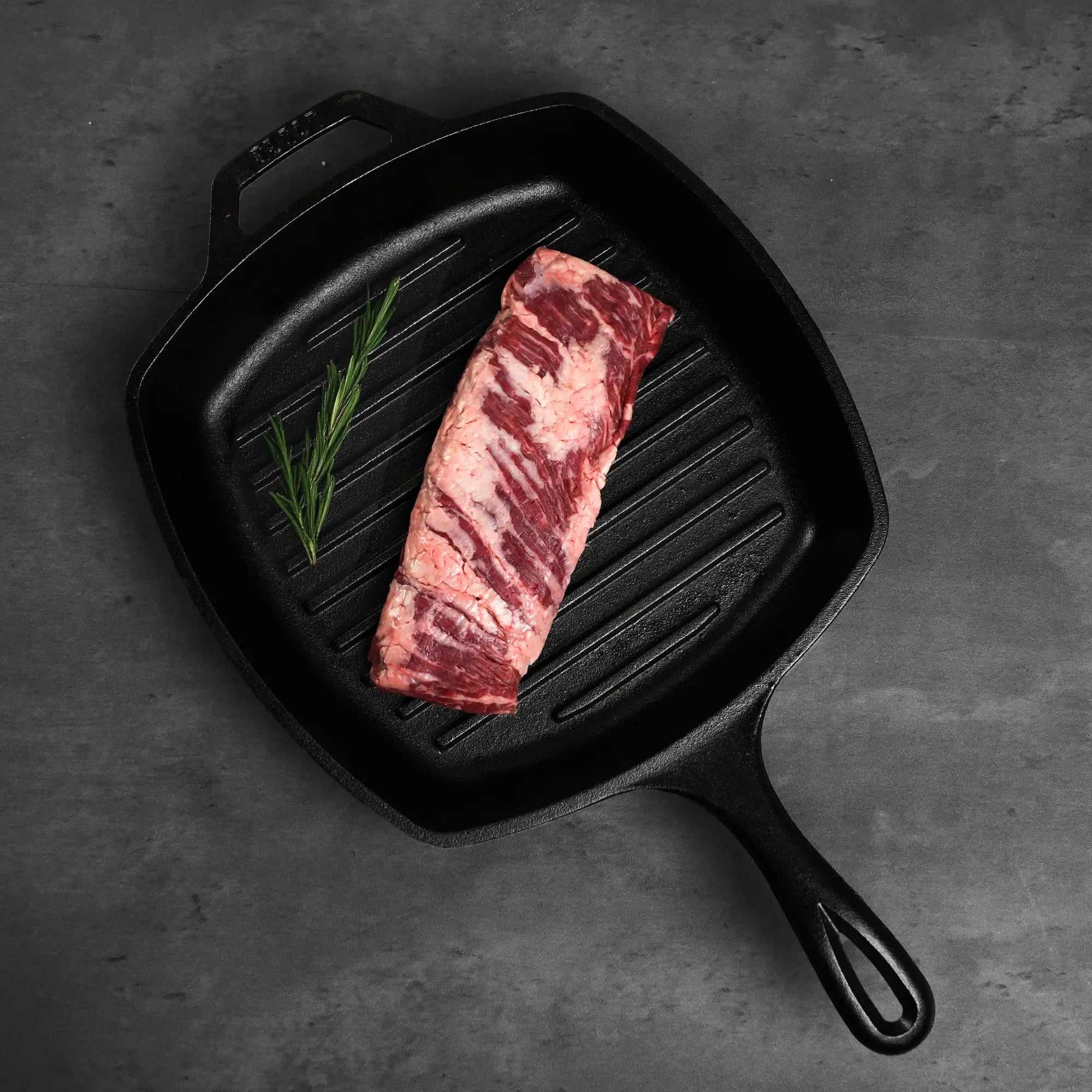 Prime Skirt Steak in a cast-iron grill pan, showcasing its marbling with a fresh rosemary sprig, ready for quick, high-heat cooking.