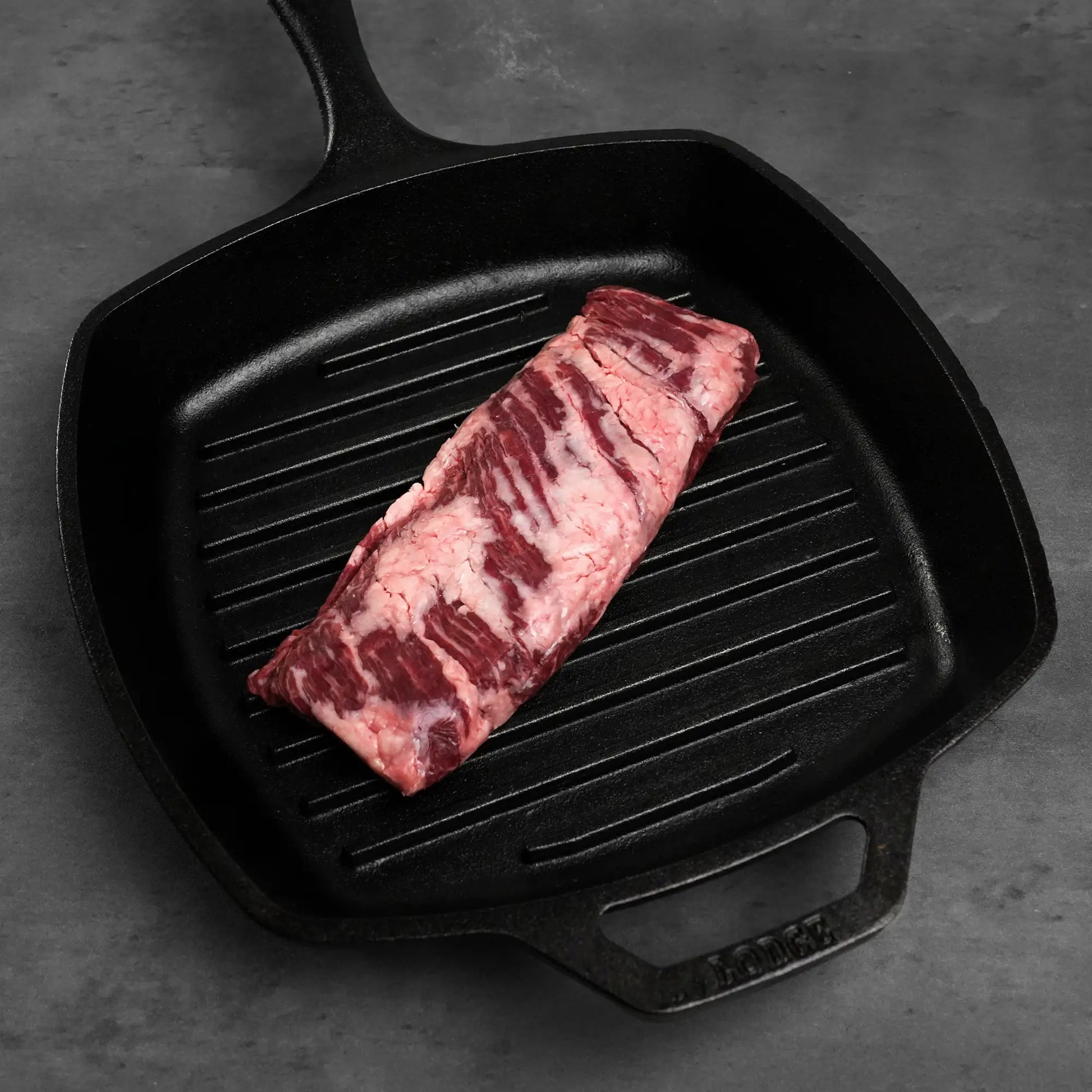 Prime Skirt Steak resting in a ridged cast-iron grill pan, showcasing its thick grain texture, ideal for quick, high-heat cooking to achieve medium-rare perfection.