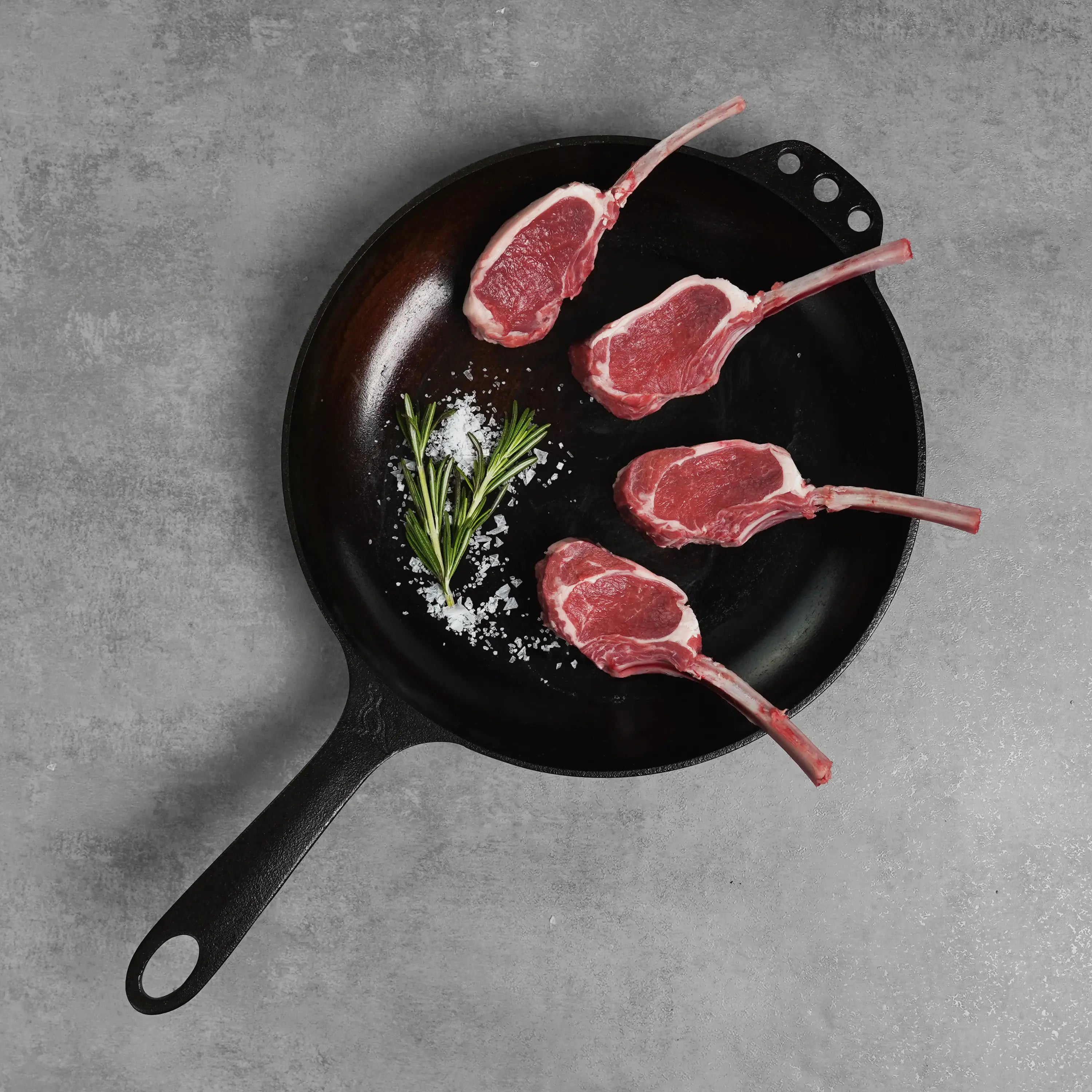 Allen Brothers Two Bite Lollipop Lamb Chops Raw on black pan with salt and garnish