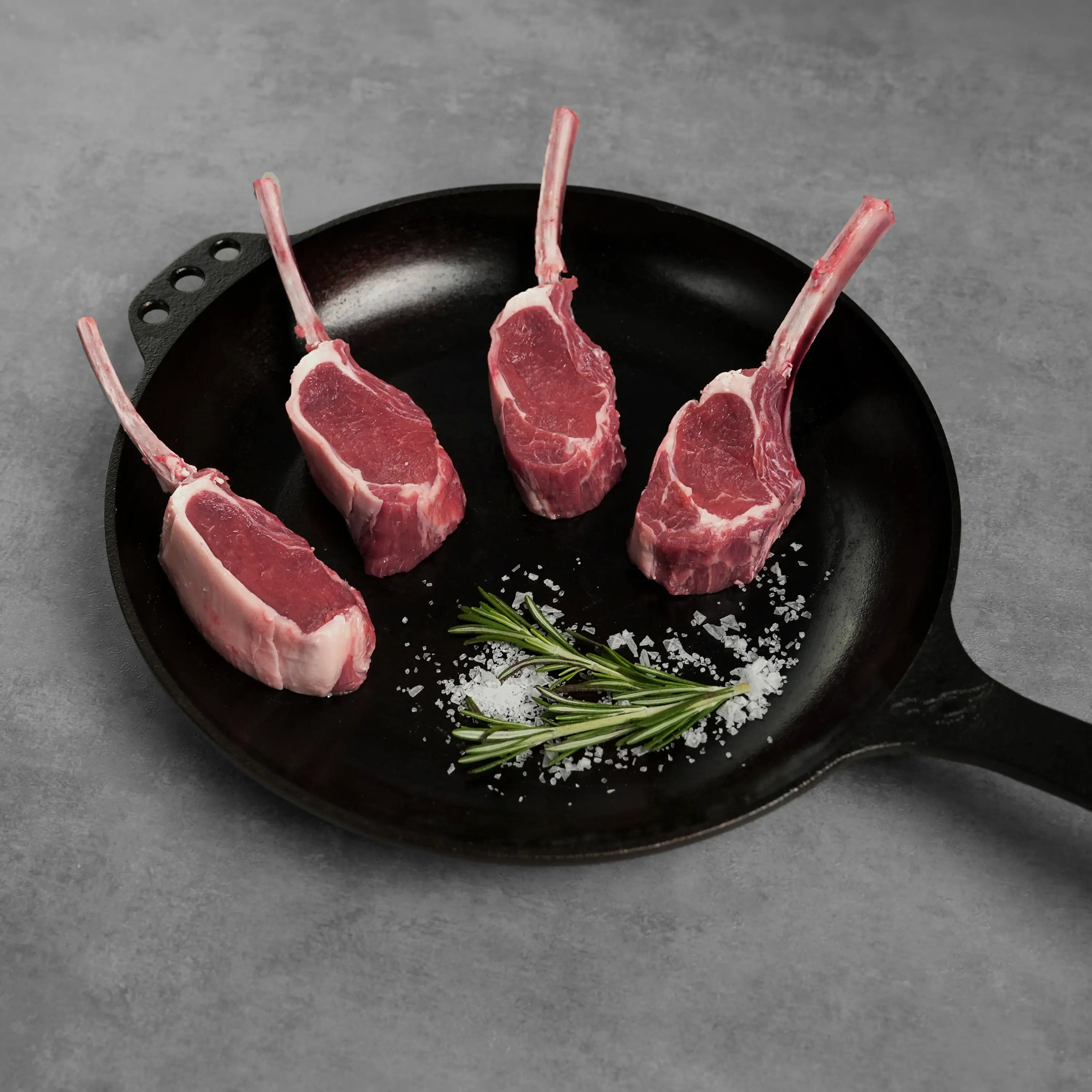 Allen Brothers Two Bite Lollipop Lamb Chops Raw on black pan with salt and garnish