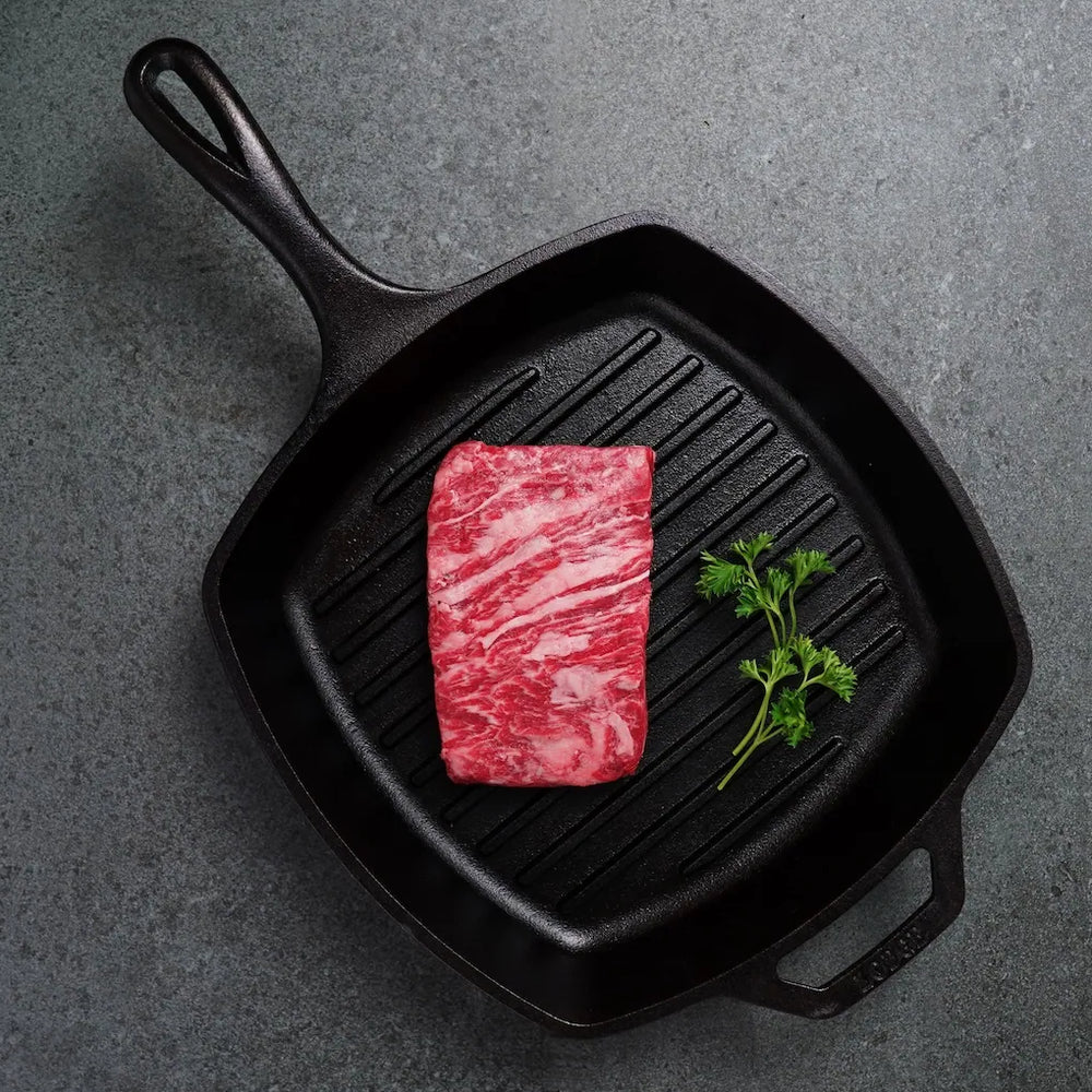 Westholme Australian Wagyu Bavette Steak in a cast-iron grill pan, showcasing its marbled texture and accompanied by fresh parsley, ready for high-heat cooking.