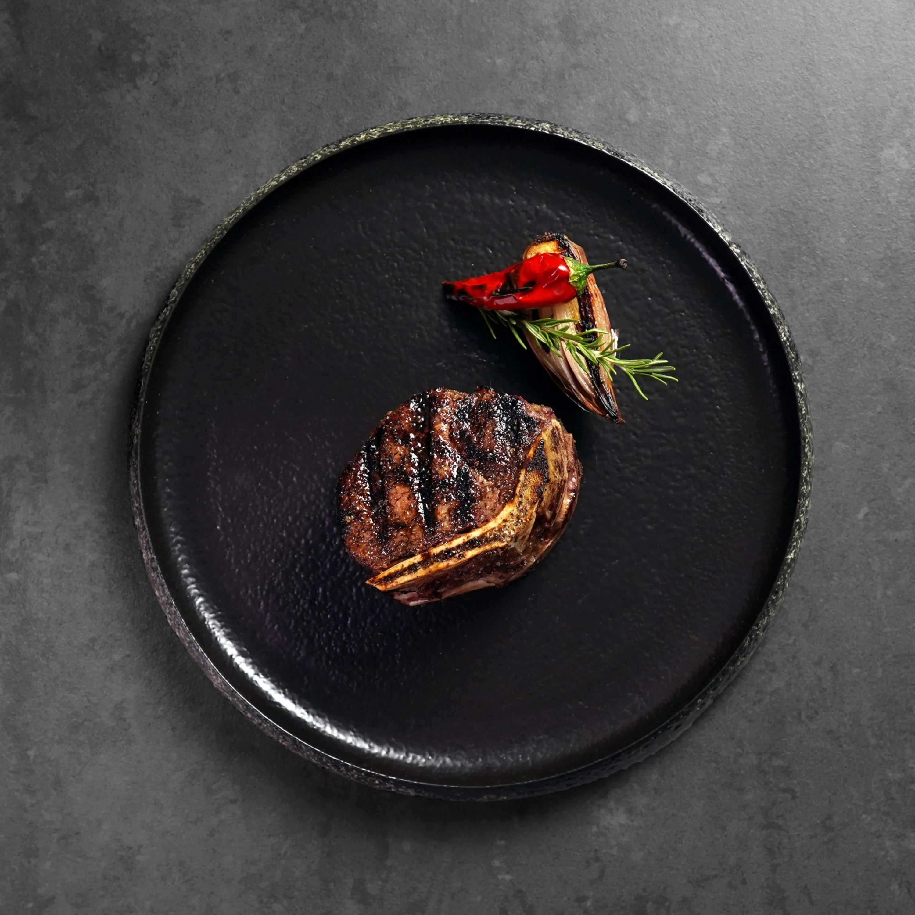 cooked steak on dark plate with red garnish