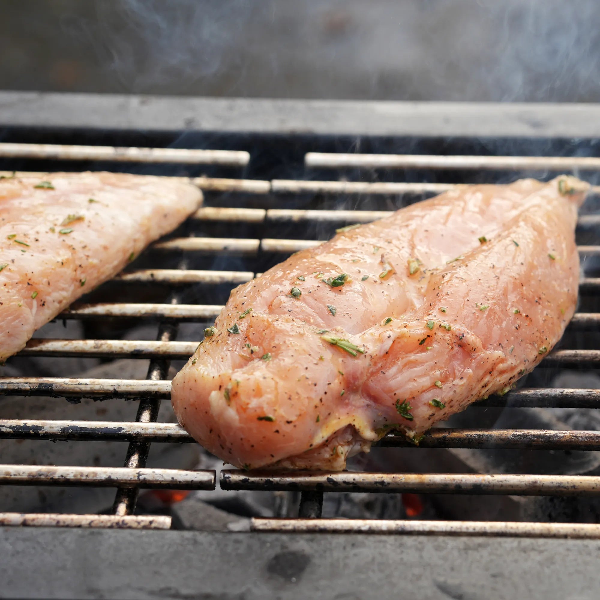 Natural Boneless Skinless Chicken Breast grilling over hot coals, releasing a wisp of smoke, reflecting quality care and stress-free farming practices.