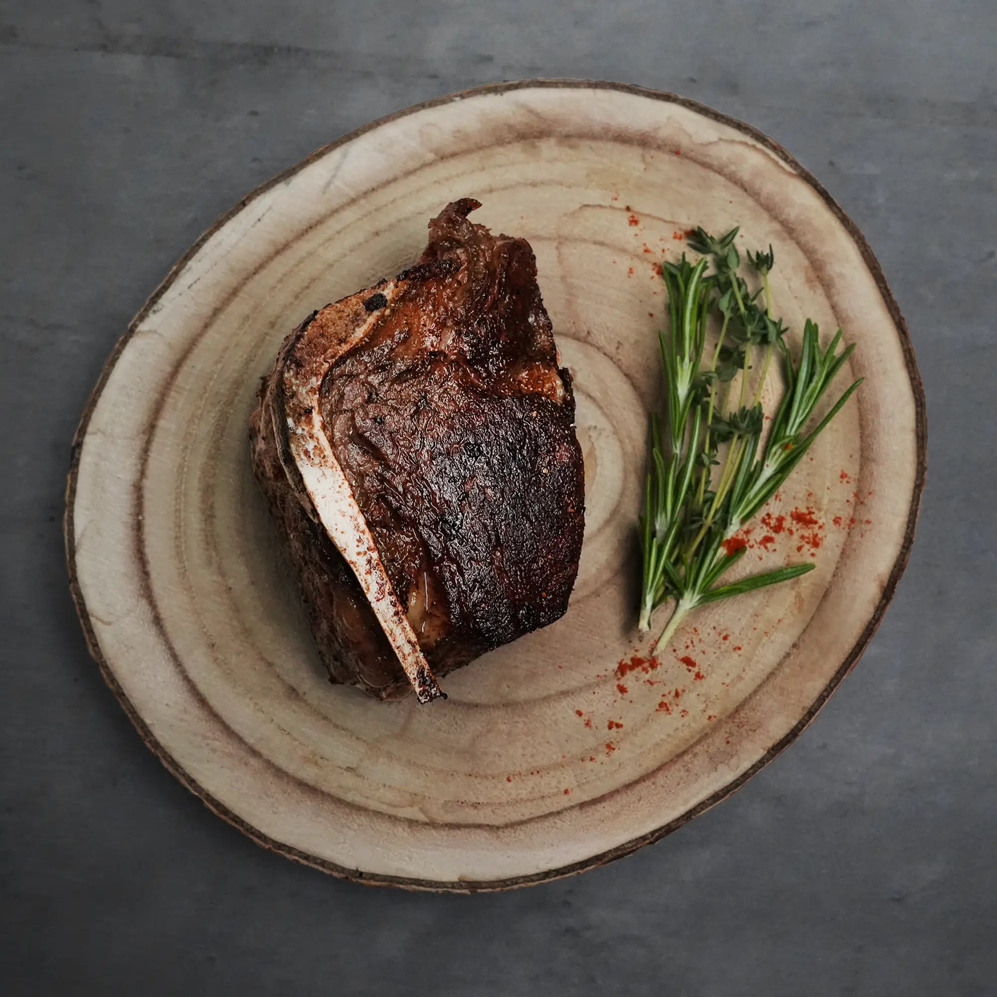 Choice Bone-In Filet Mignon on a wooden platter with fresh herbs and red spices, showcasing its steakhouse-quality cut, bone-in richness, and tender juiciness.