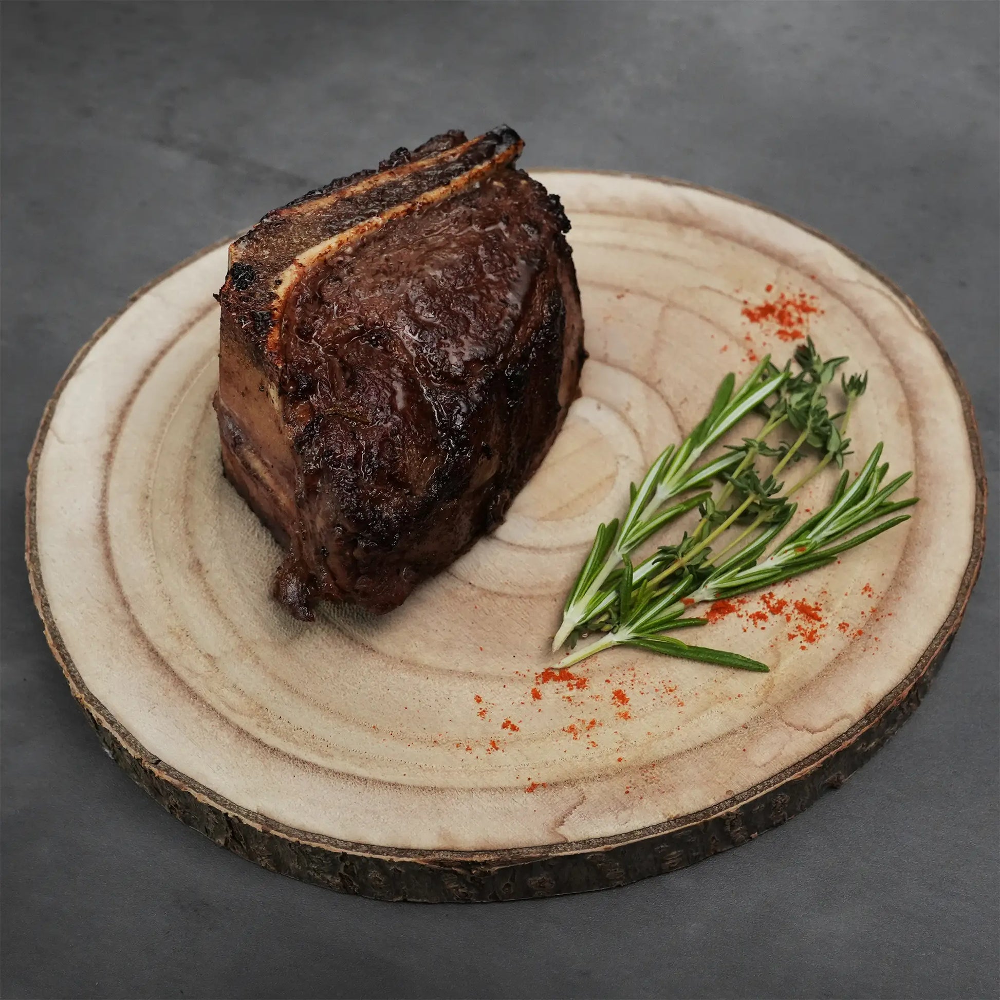 Choice Bone-In Filet Mignon on a rustic wood board, garnished with rosemary, thyme, and red spice, highlighting its wet-aged, steakhouse-quality tenderness and flavor.