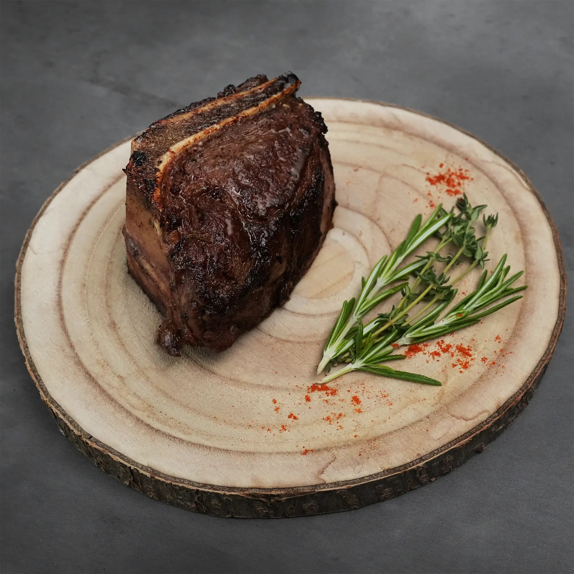 Choice Bone-In Filet Mignon on a rustic wood board, garnished with rosemary, thyme, and red spice, highlighting its wet-aged, steakhouse-quality tenderness and flavor.