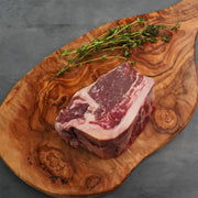 Choice Bone-In Filet Mignon on rustic board, well-marbled and wet-aged, accompanied by thyme sprigs, promising steakhouse quality with tender, juicy texture.
